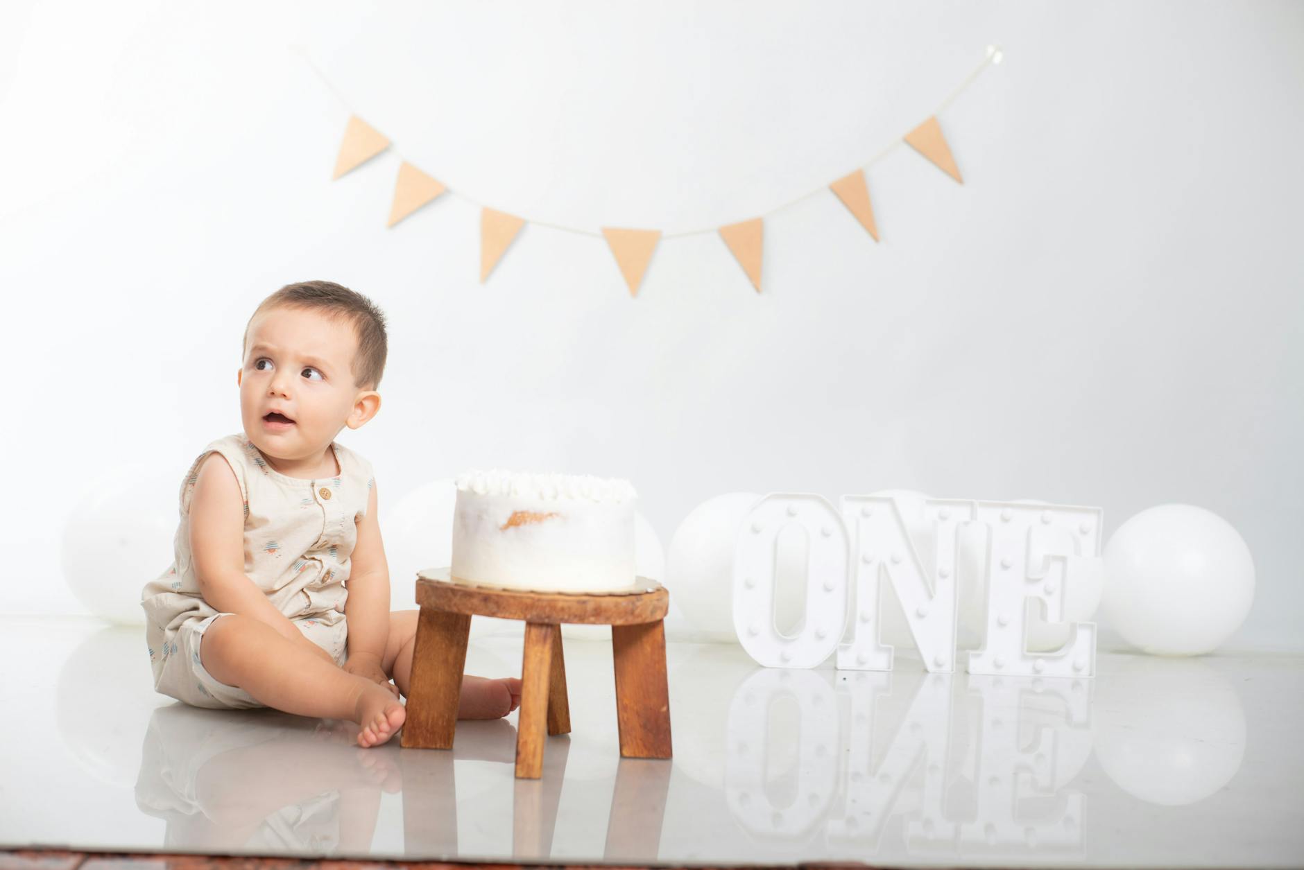 Adorable baby sitting by a birthday cake with a festive decoration celebrating the first birthday. - child developmental milestones