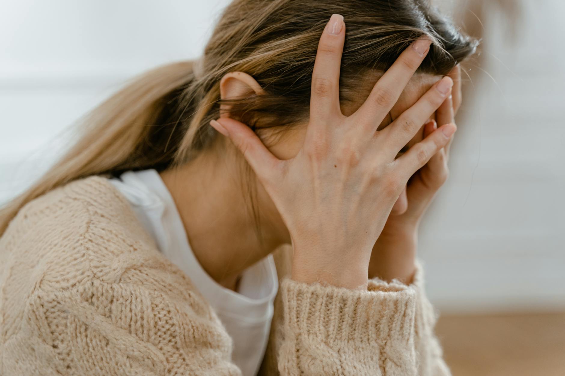 Woman sitting indoors with face covered by hands, expressing stress and frustration. - coping with spring anxiety