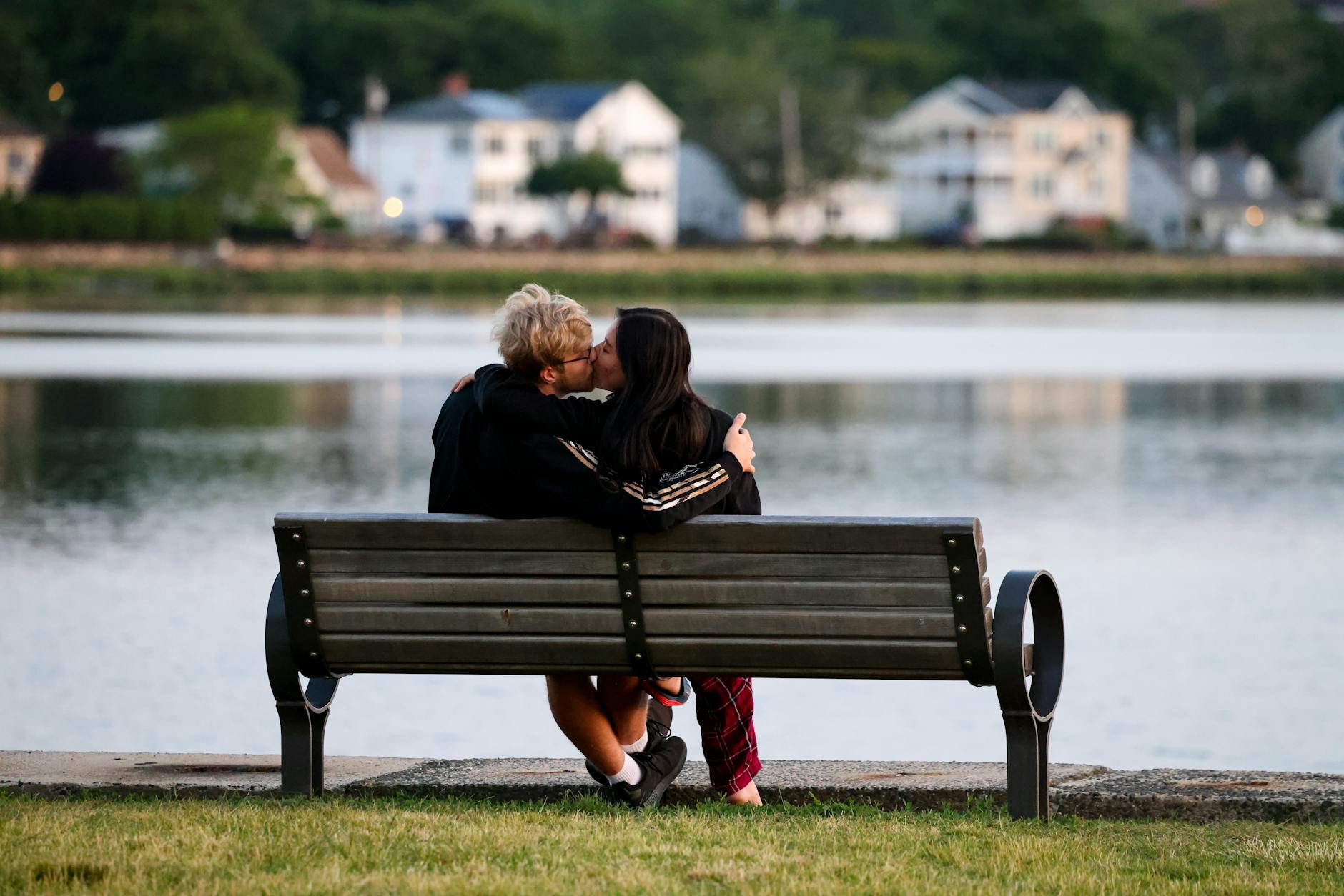 A couple lovingly kisses on a bench with a serene lake backdrop. - couples spring reconnection