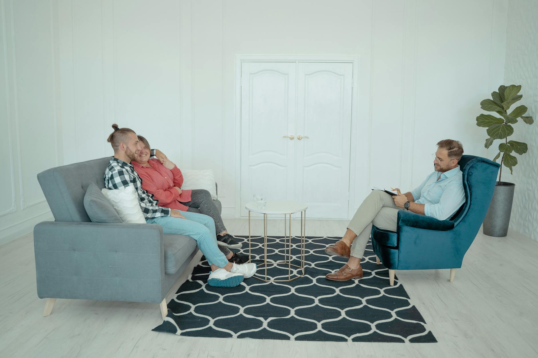 A married couple sits with a counselor discussing relationship issues in a modern office setting. - couples therapy february