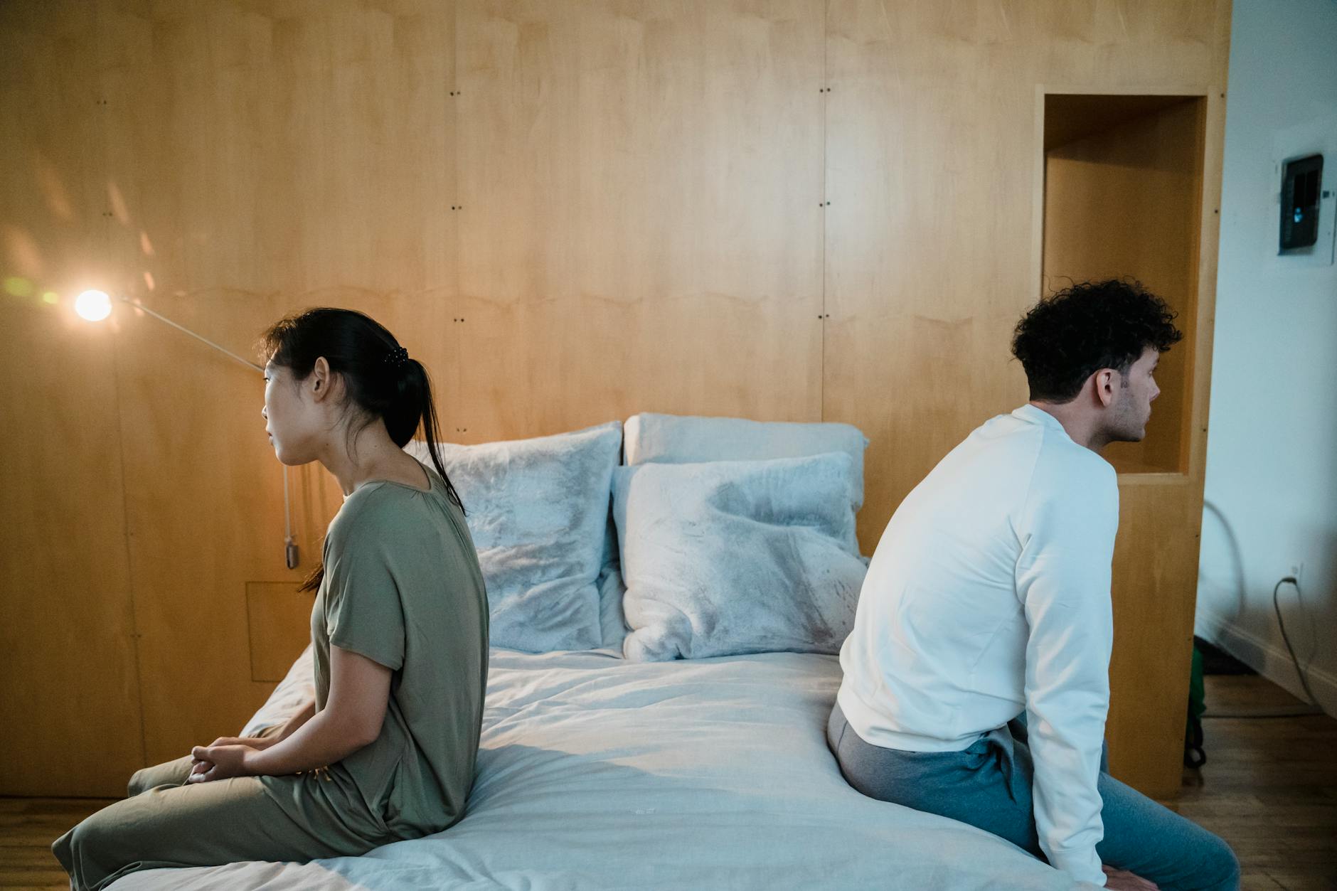 A couple sits back to back on a bed, showing tension and misunderstanding in a cozy bedroom. - couples therapy intimacy