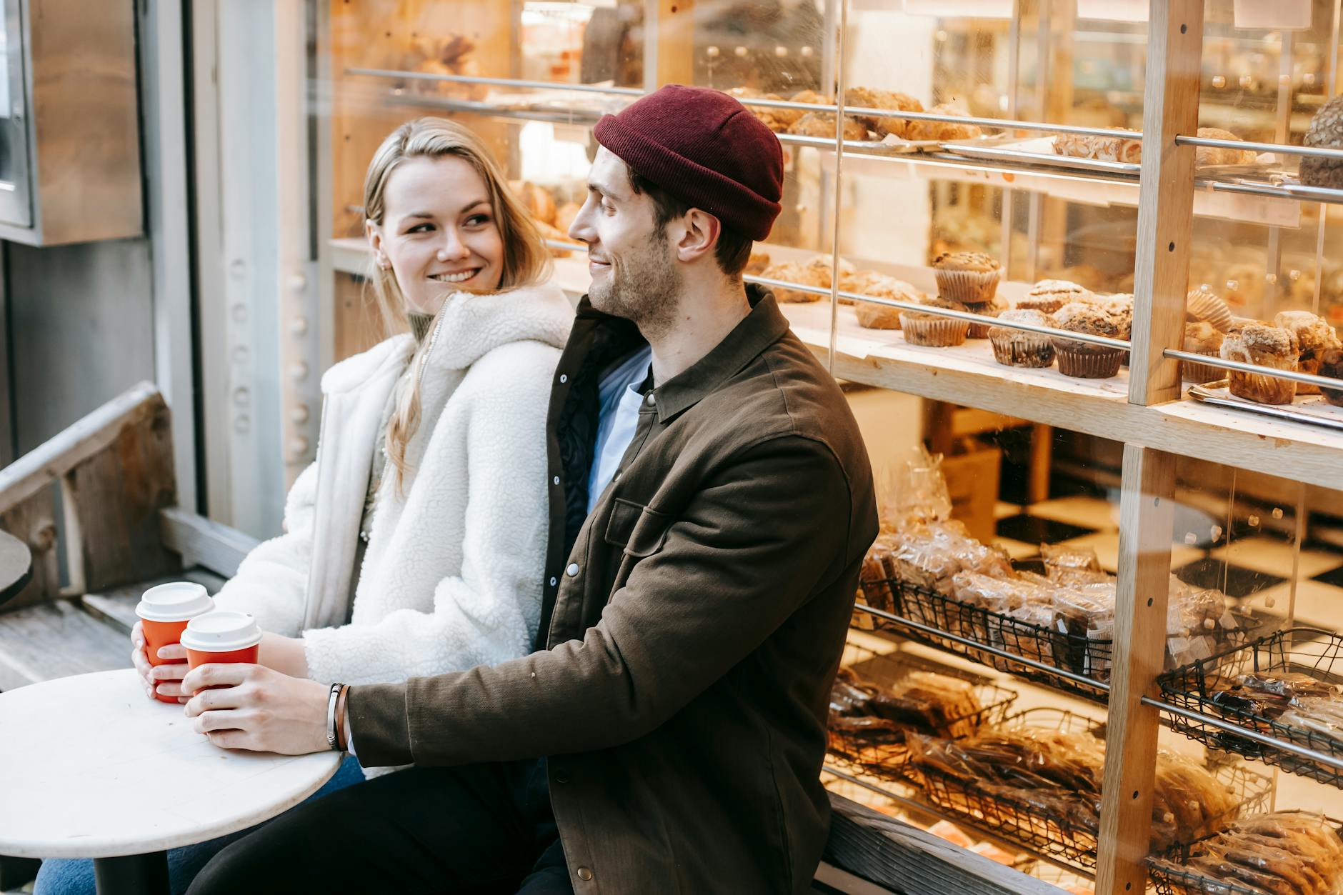 Cheerful young couple in casual clothes sitting at table with paper cups with hot beverage and looking at each other - dating after long break