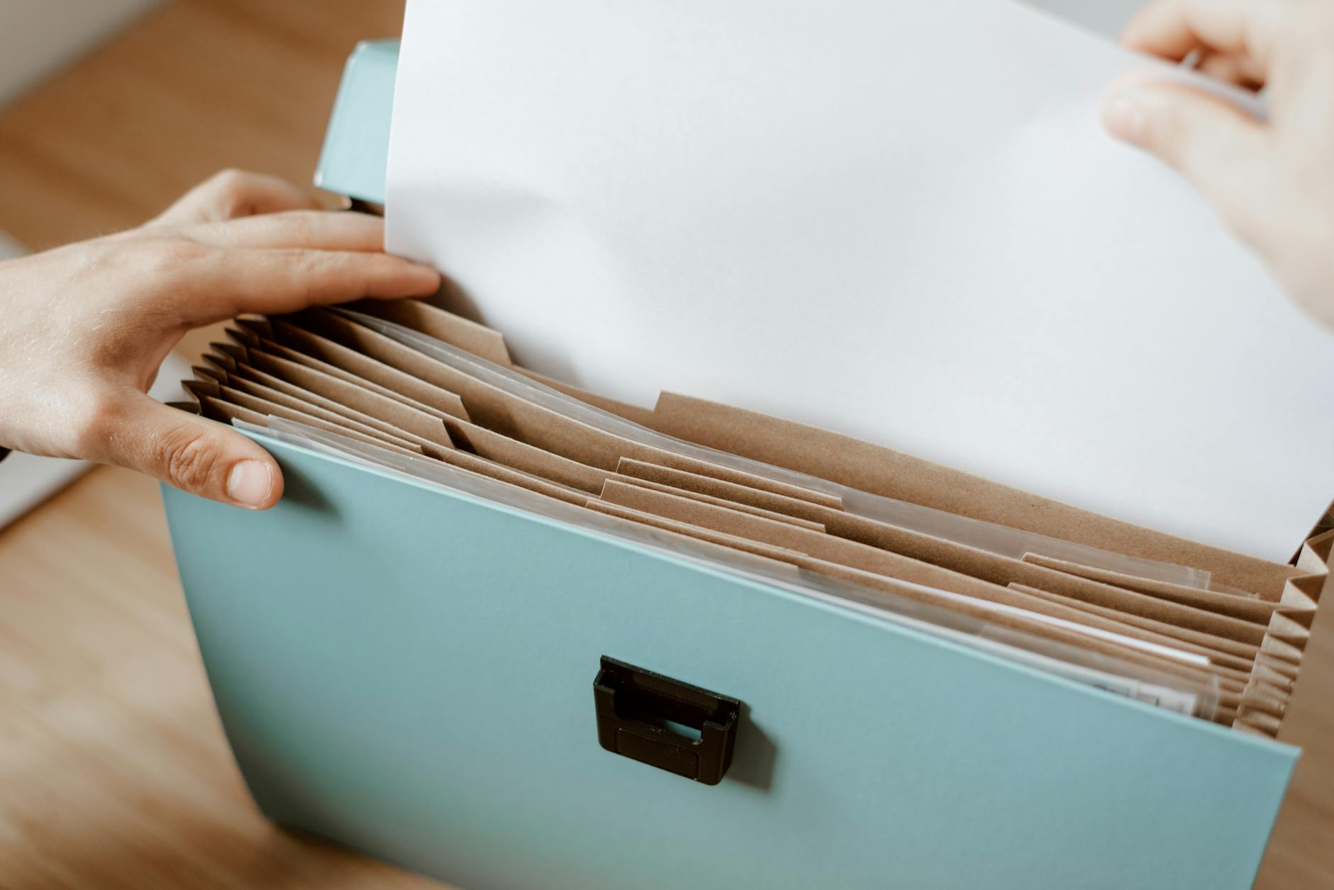 Hands organizing papers in a blue office folder with brown dividers, showing workplace efficiency. - declutter emotional baggage