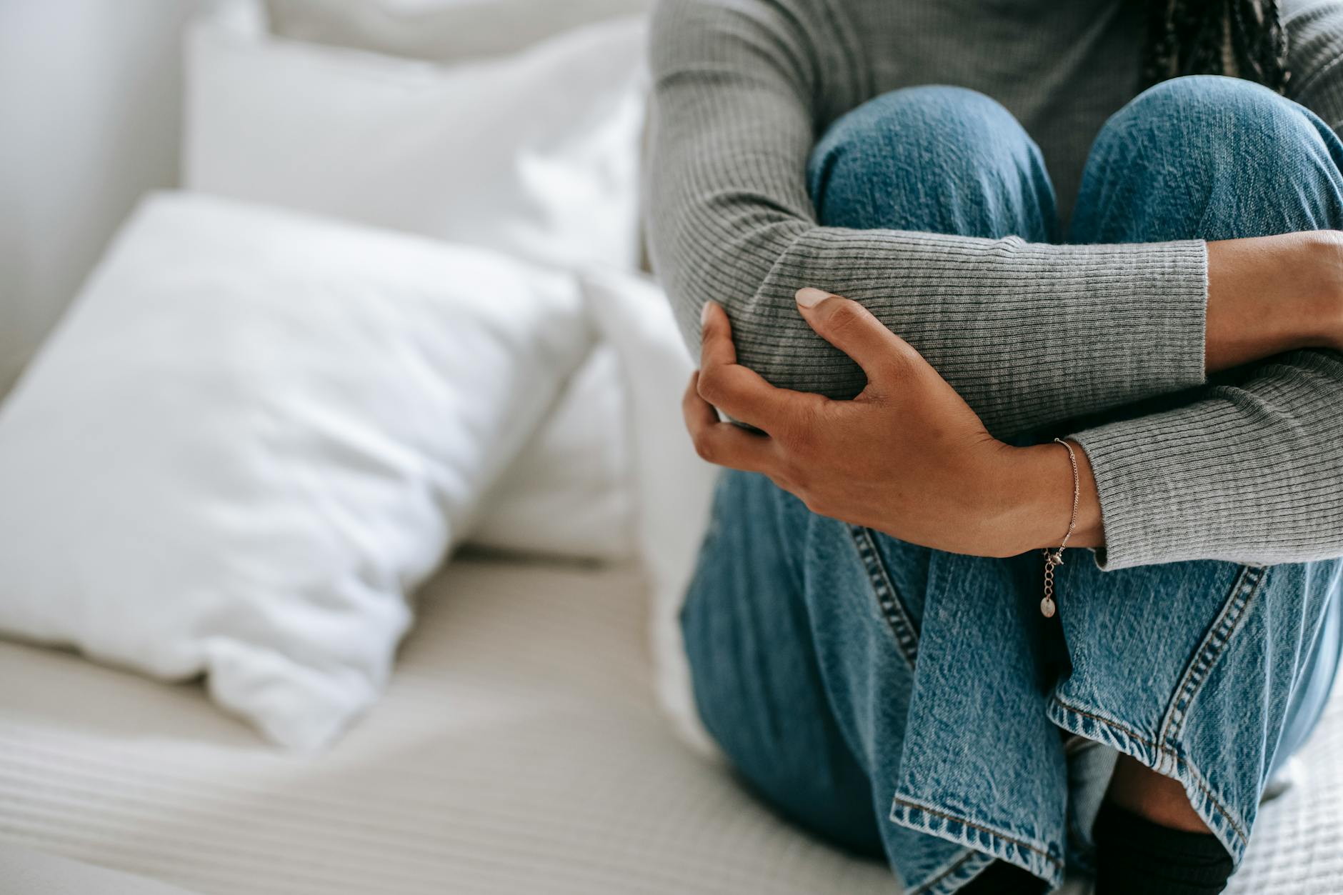 Crop faceless female feeling helpless and frustrated embracing knees while sitting on bed in loneliness - declutter negative thoughts