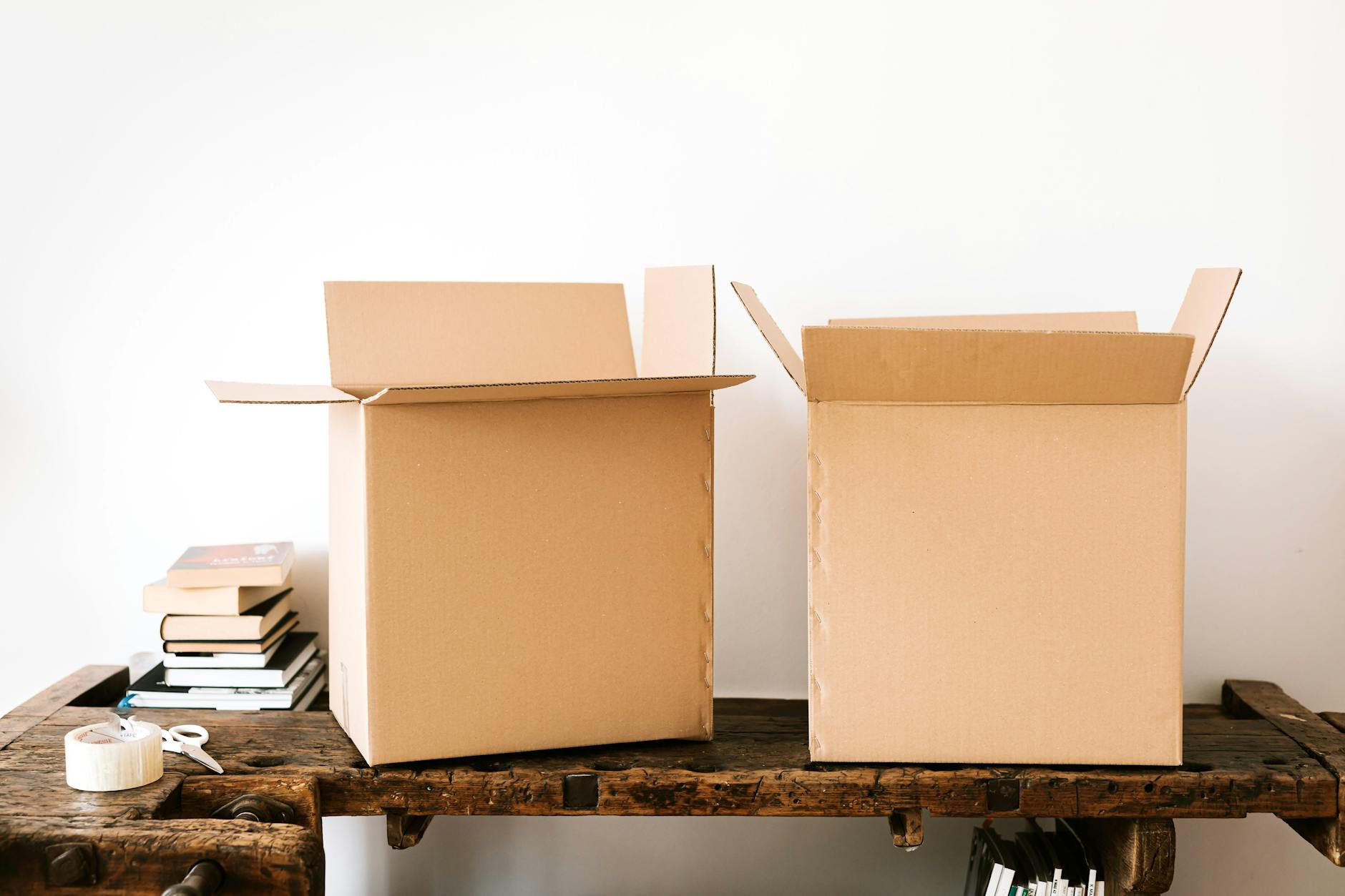 Opened carton boxes and stacked books placed on shabby wooden desk with tape against white wall - declutter negative thoughts