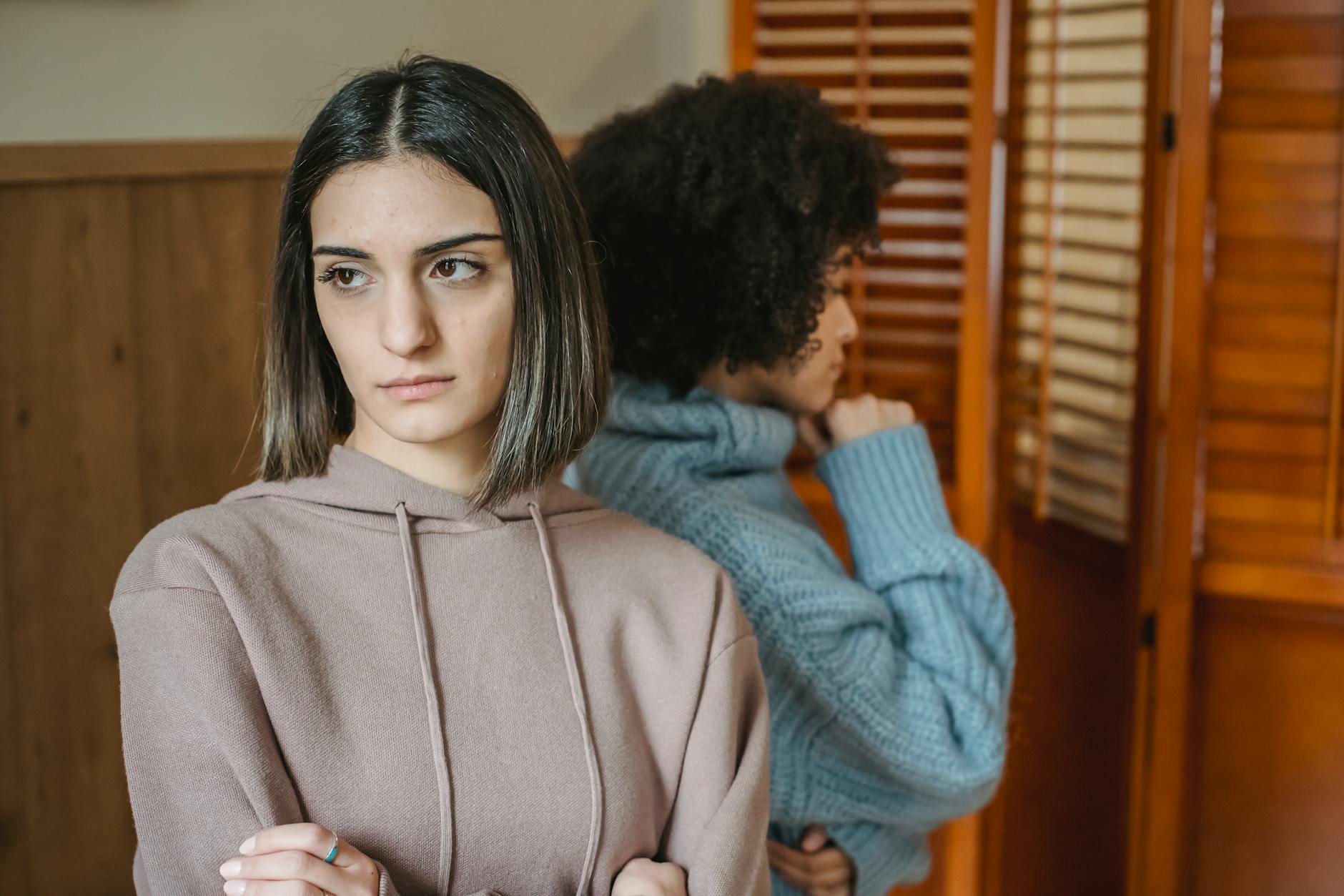 Upset multiracial women in casual wear standing in light room near wall with wooden folding screen while having conflict at home - difficult conversations