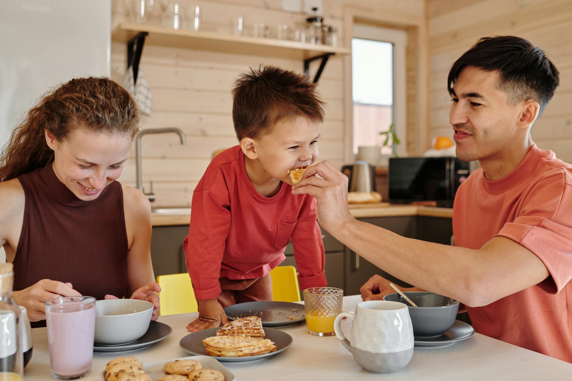 A joyful family of three shares breakfast in a cozy kitchen setting, depicting warmth and togetherness. - family routines with kids