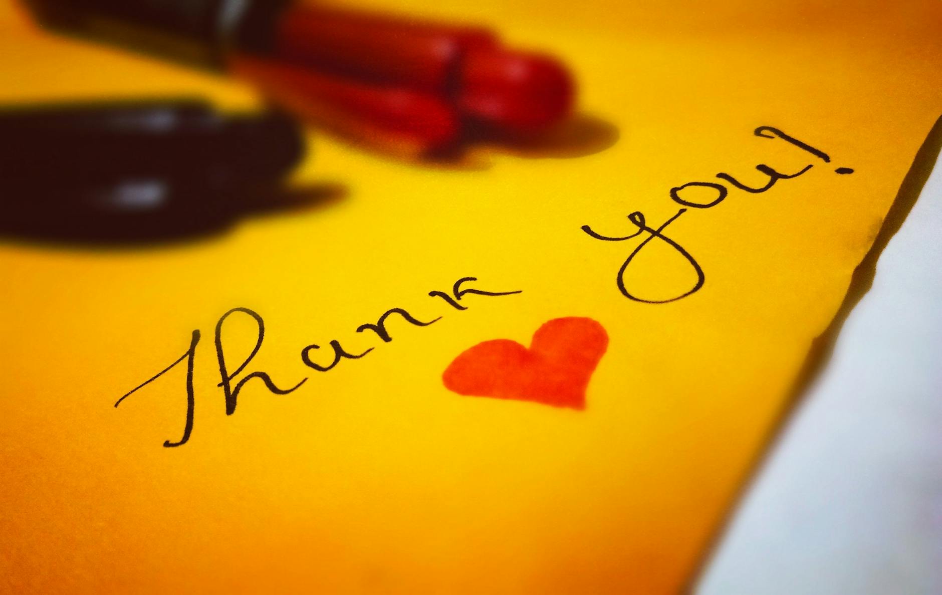 Close-up of a thank you note with a heart and pen on colored paper. - gratitude practices winter