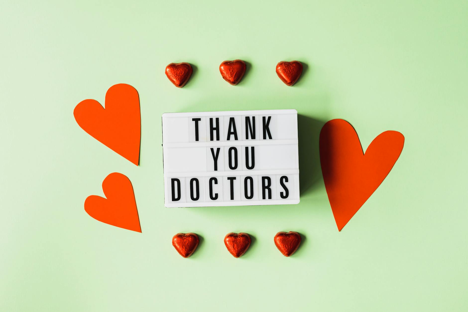 Top view of red heart shaped decorative elements and white retro light box with THANK YOU DOCTORS gratitude message arranged on green background - gratitude practices winter