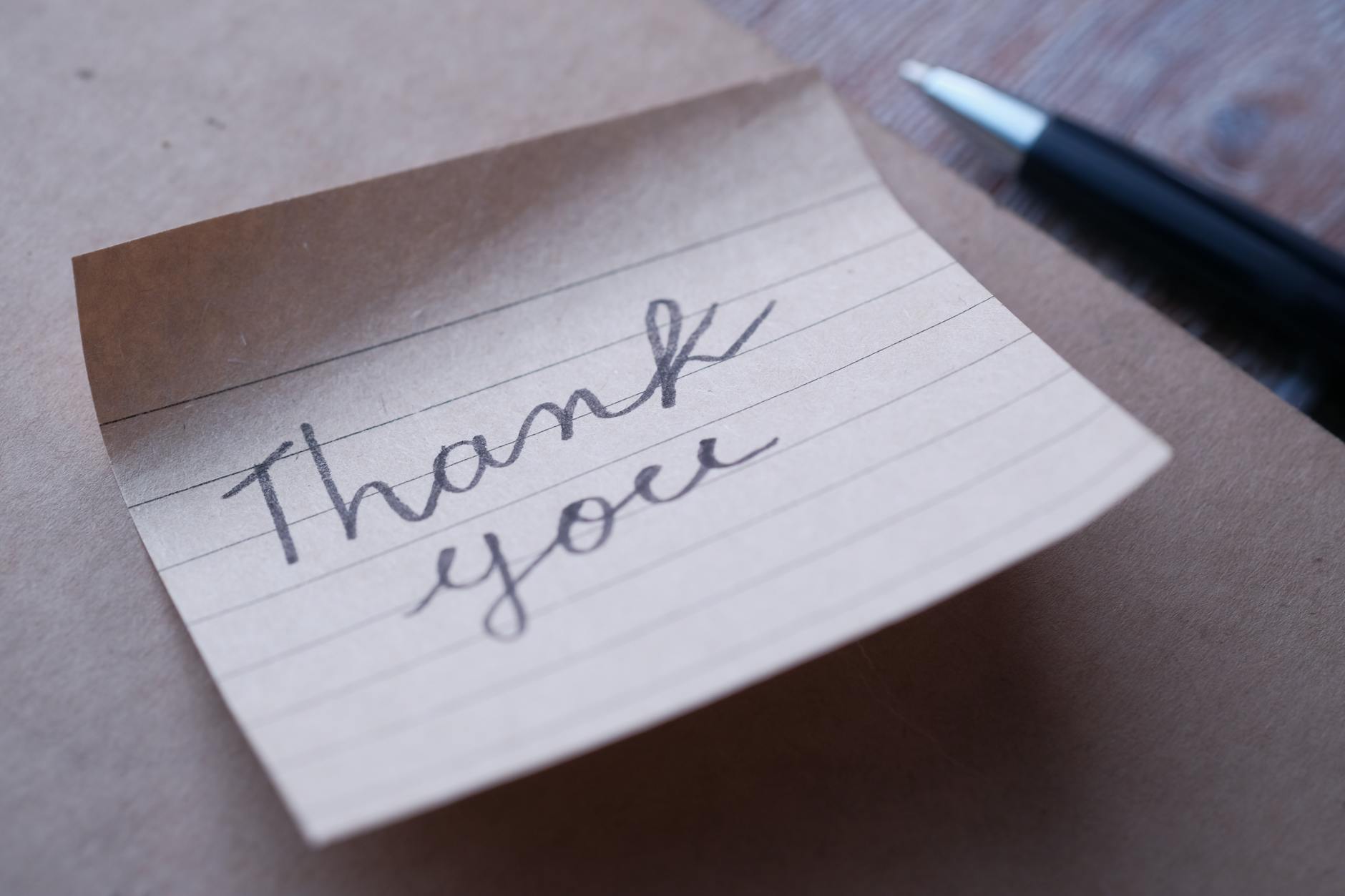 Close-up of a handwritten thank you note on brown paper with a pen nearby. - gratitude practices winter