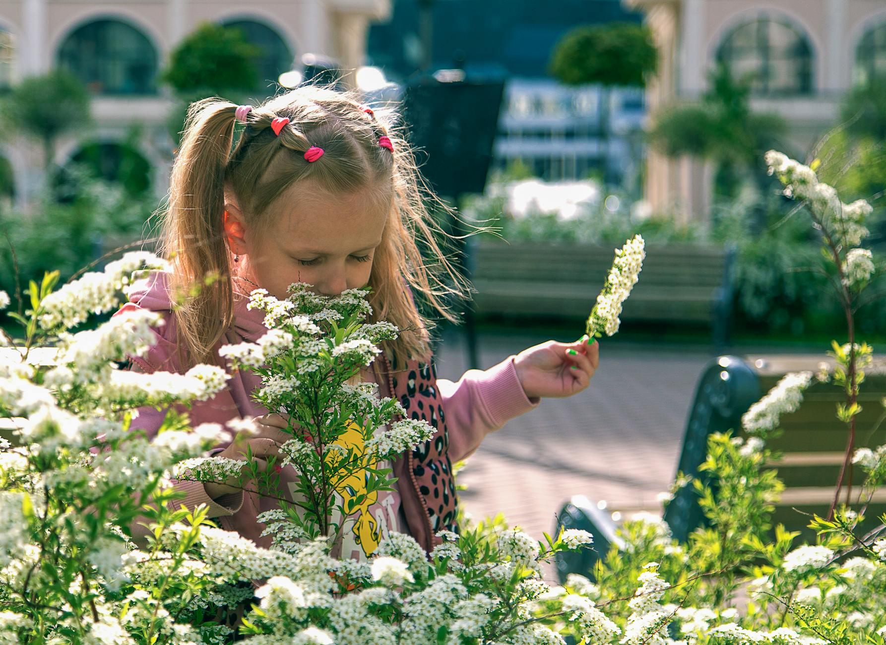 A little girl in a pink hoodie admires white flowers in an urban garden, capturing a moment of serene childhood wonder. - kids spring gardening