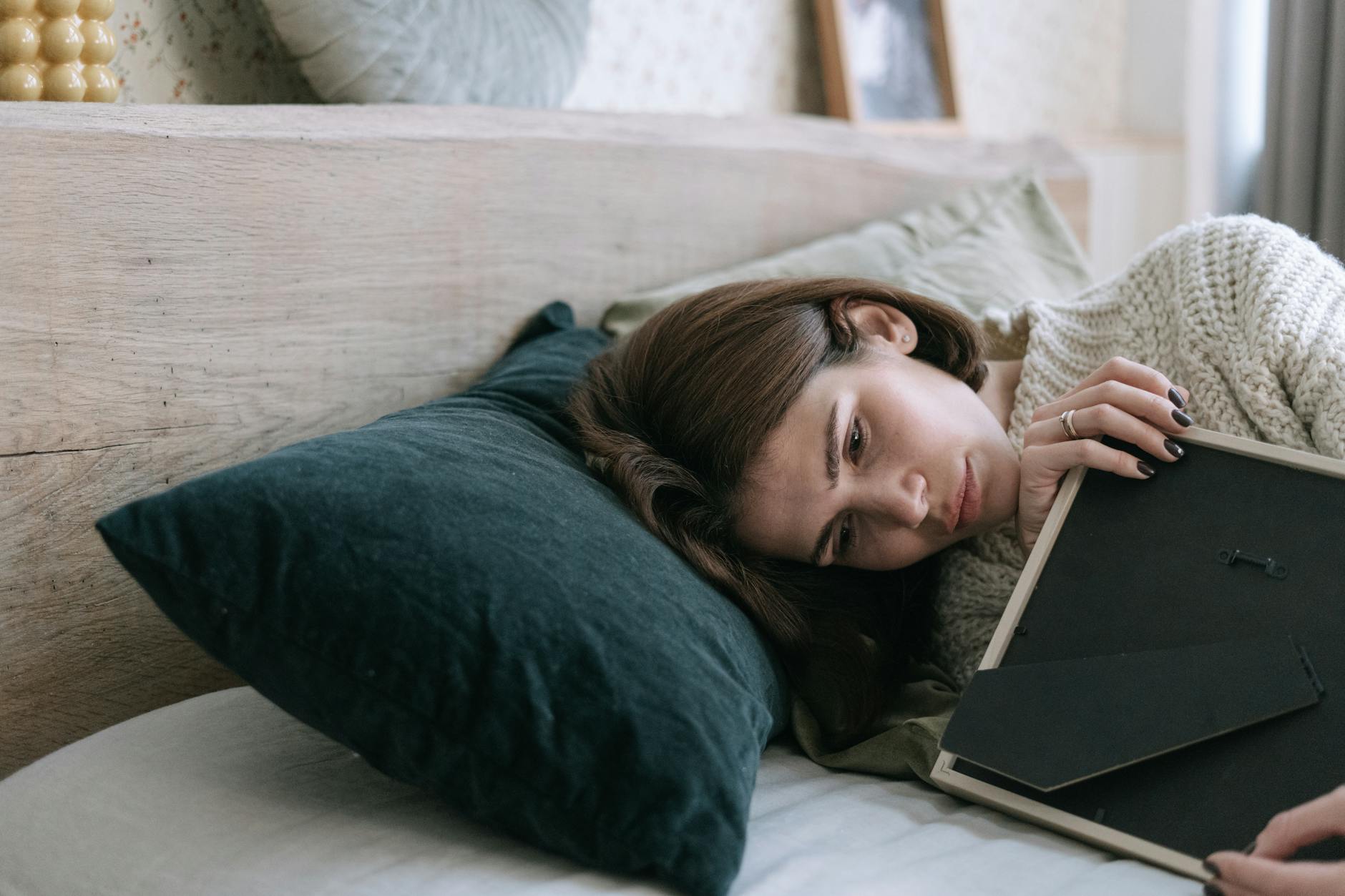 Woman lying in bed holding a picture frame, reflecting quietly indoors. - let go of past hurts