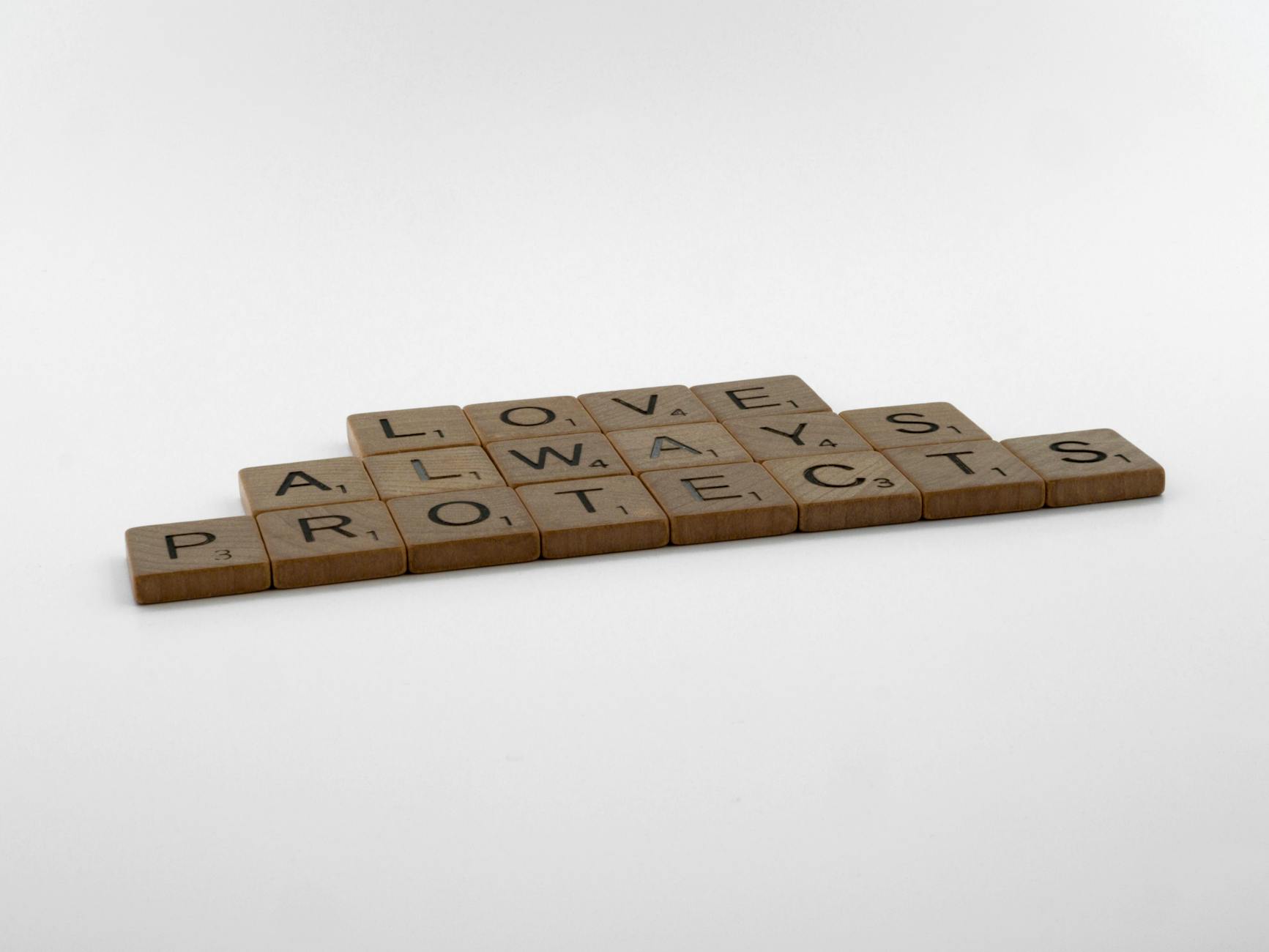 Close-up of Scrabble tiles on white surface spelling 'Love Always Protects'. - love languages explained