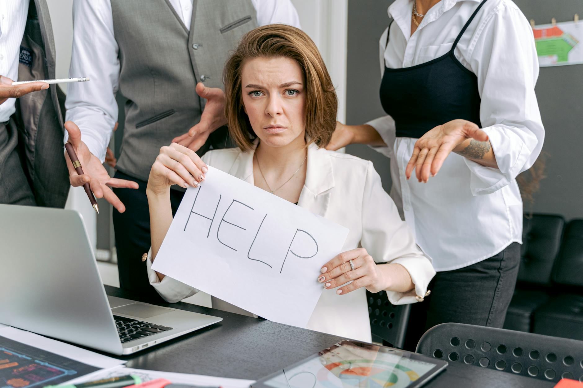 Stressed office worker holding a help sign surrounded by colleagues' demands. - manage overwhelm cbt