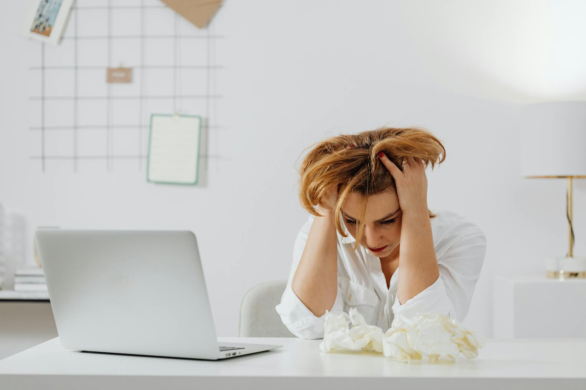 Frustrated woman in white shirt at desk with laptop, feeling overwhelmed. - manage overwhelm cbt