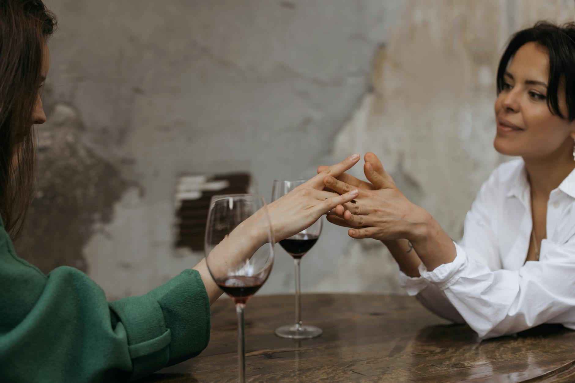 Two women share an intimate moment over red wine, holding hands in a cozy setting. - marriage advice women