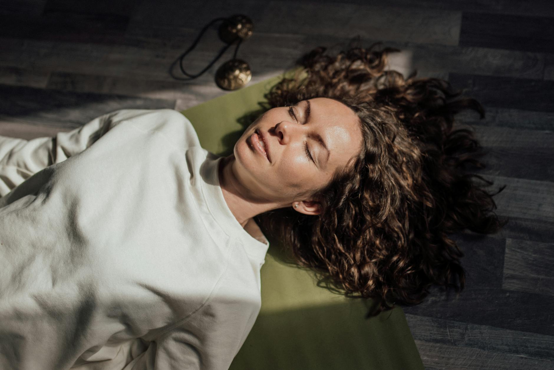 Woman with curly hair meditating on yoga mat indoors, eyes closed. - mindfulness for stress