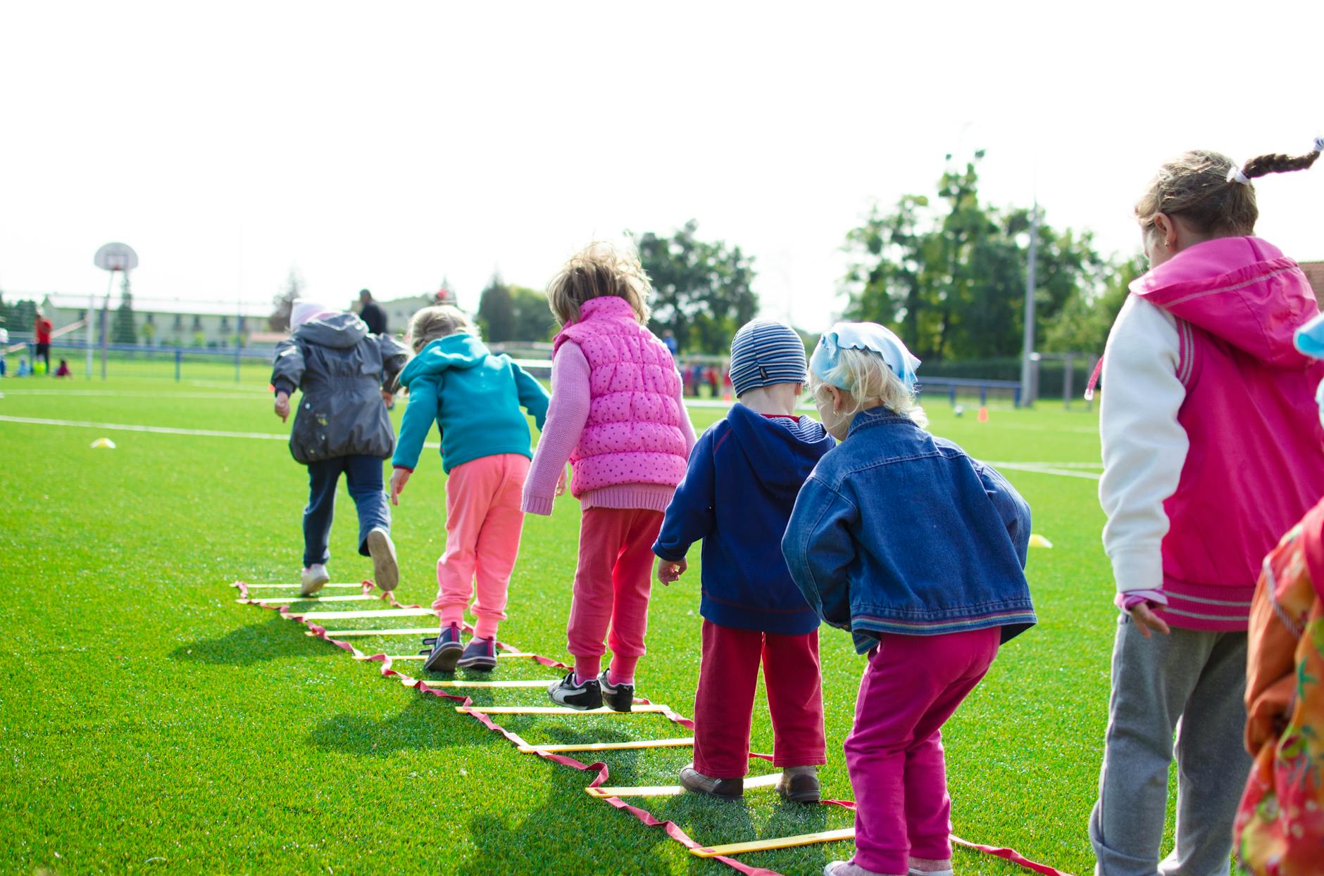 Children enjoy an outdoor activity on a grassy field, stepping over a ladder. - outdoor play benefits