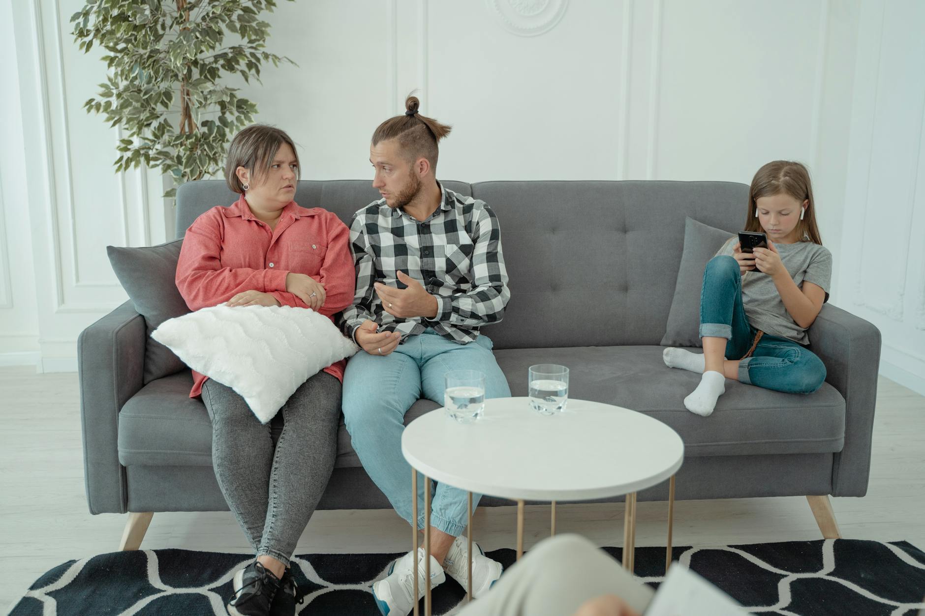 A family therapy session with parents discussing things while a child is absorbed in her smartphone. - parent child communication