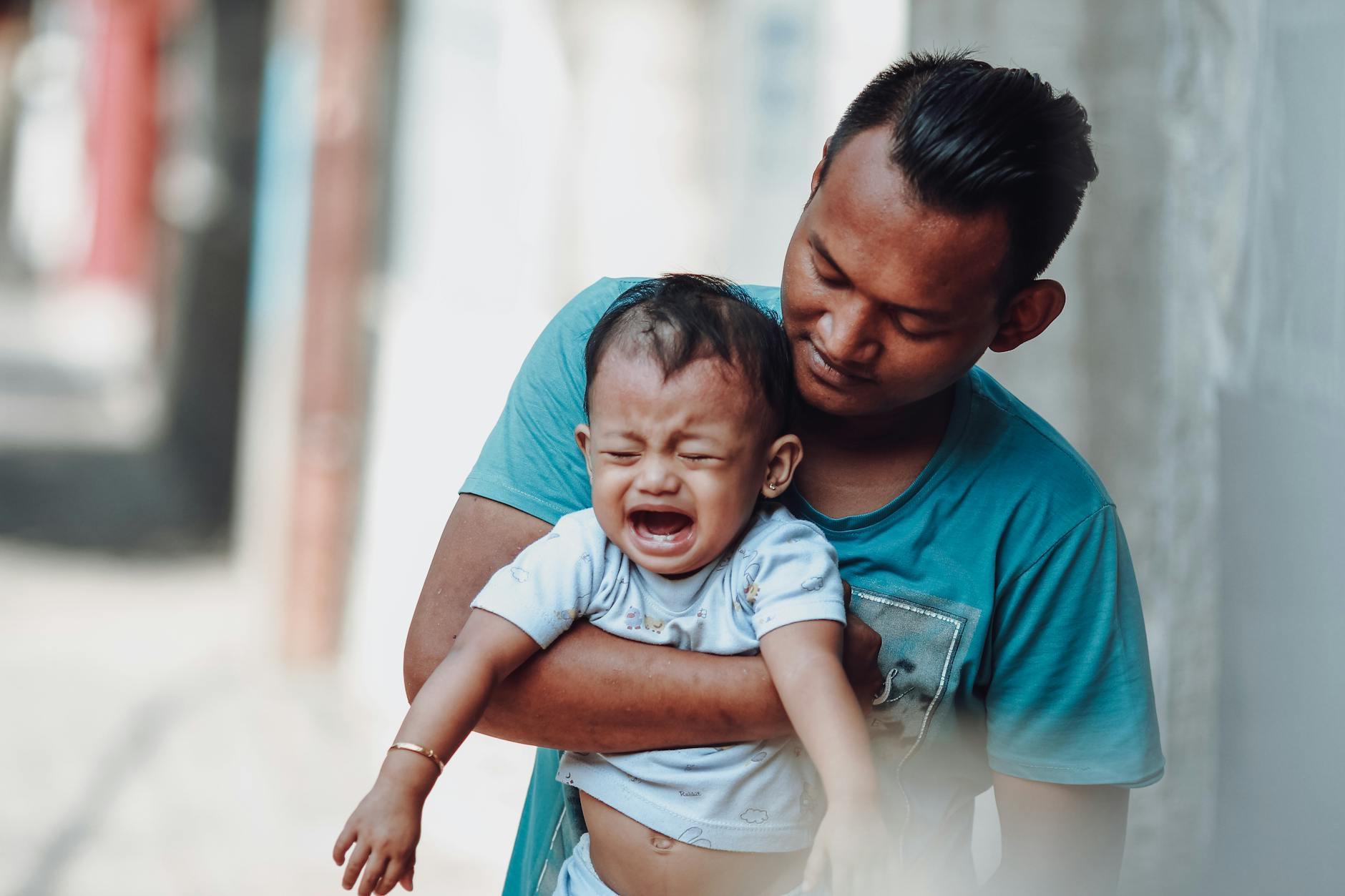 A father lovingly holds his crying baby boy outdoors, creating a tender parenting moment. - parental emotional support