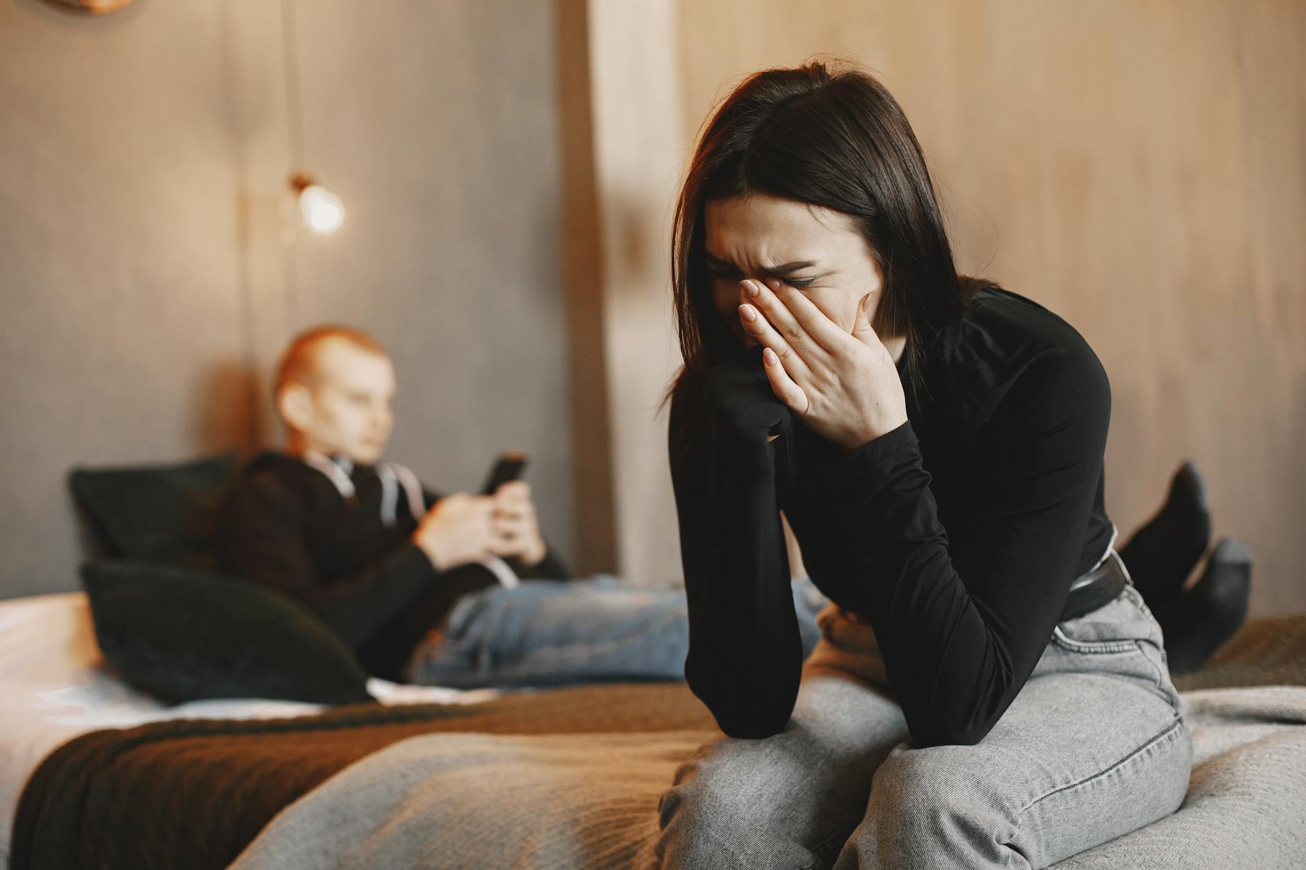 Woman crying on bed, man in background, illustrating relationship stress. - partner depression symptoms