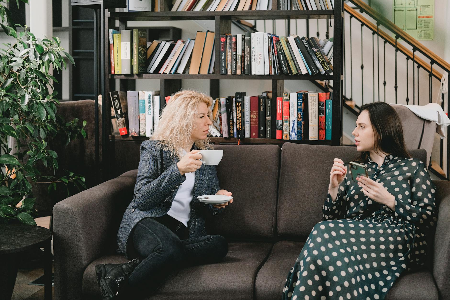 Female sitting on sofa with cup of hot drink and listening to woman during break in work - post-hibernation conversations