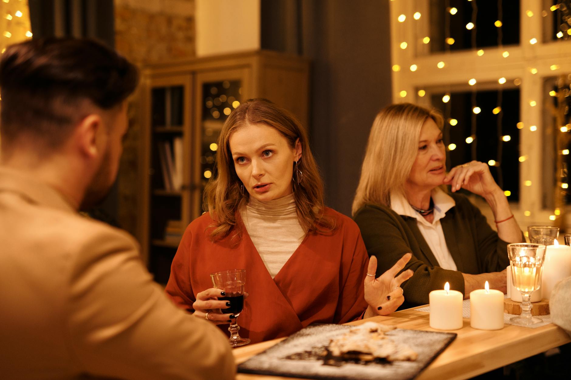 Three people enjoying a festive dinner table conversation surrounded by warm holiday lights. - post holiday family talk