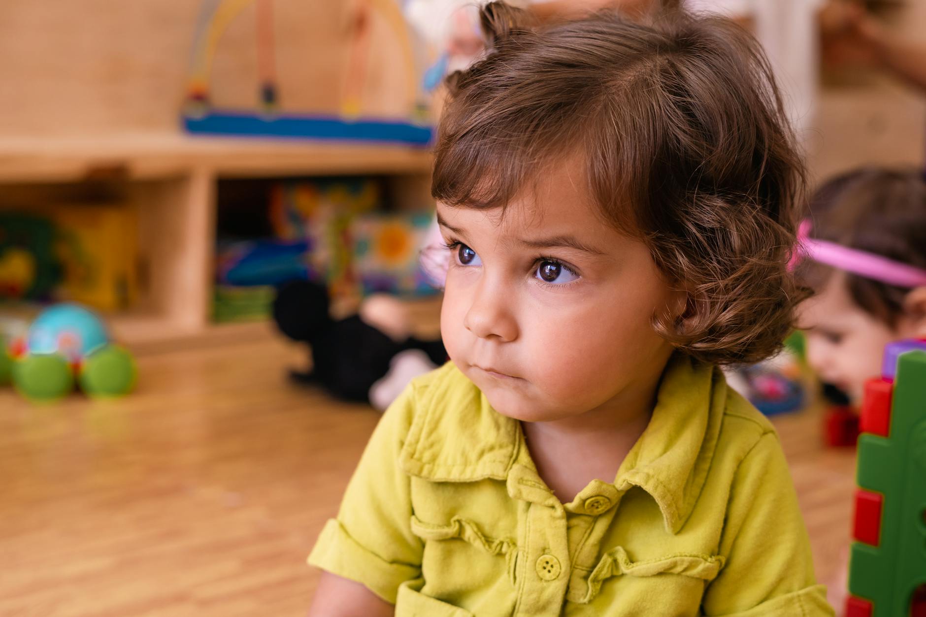 Charming toddler with curly hair in a vibrant playroom, focusing on toys. - preschool emotional intelligence