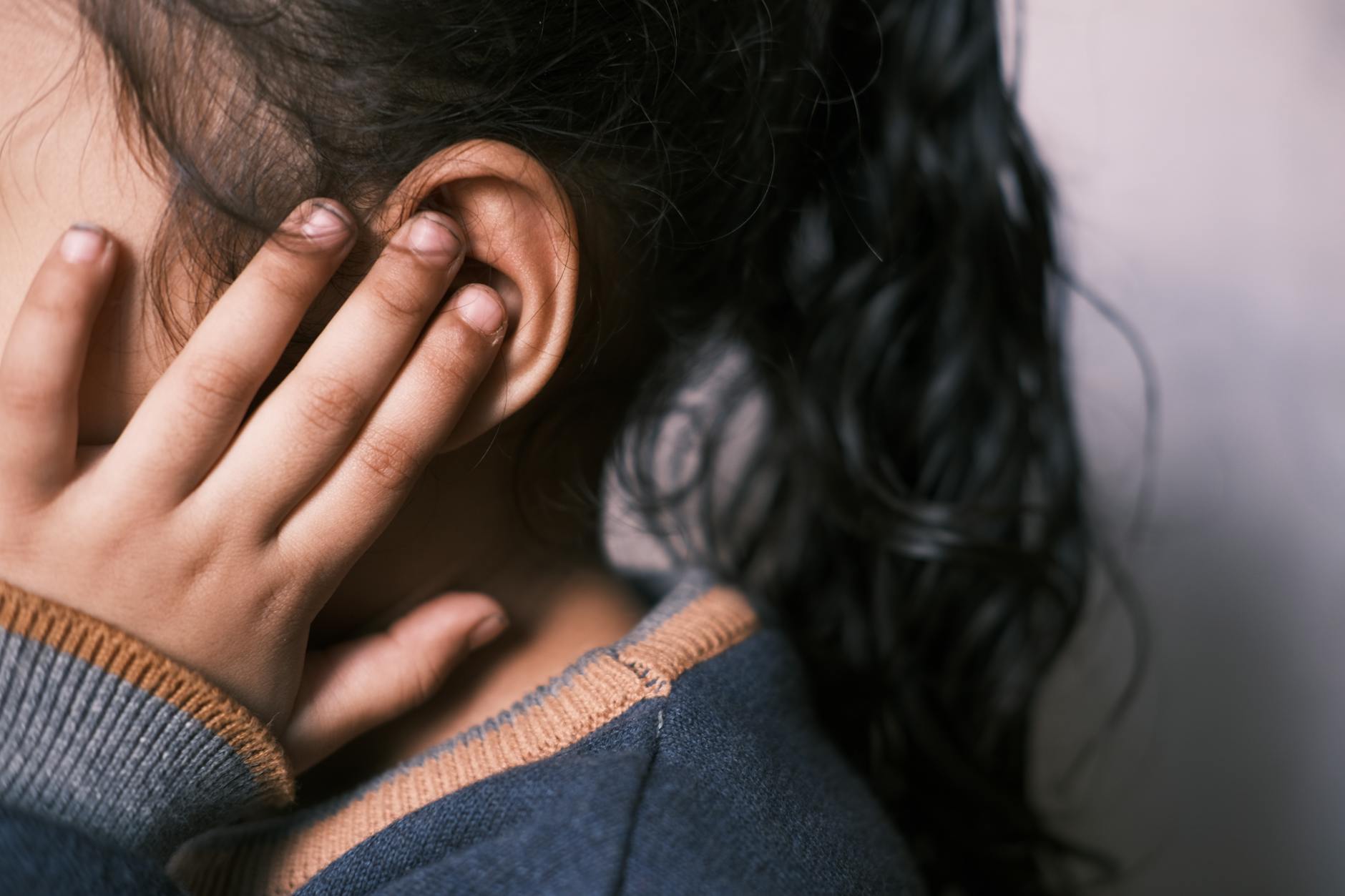 A young girl with long dark hair covering her ear in a thoughtful pose. - preschool emotional intelligence