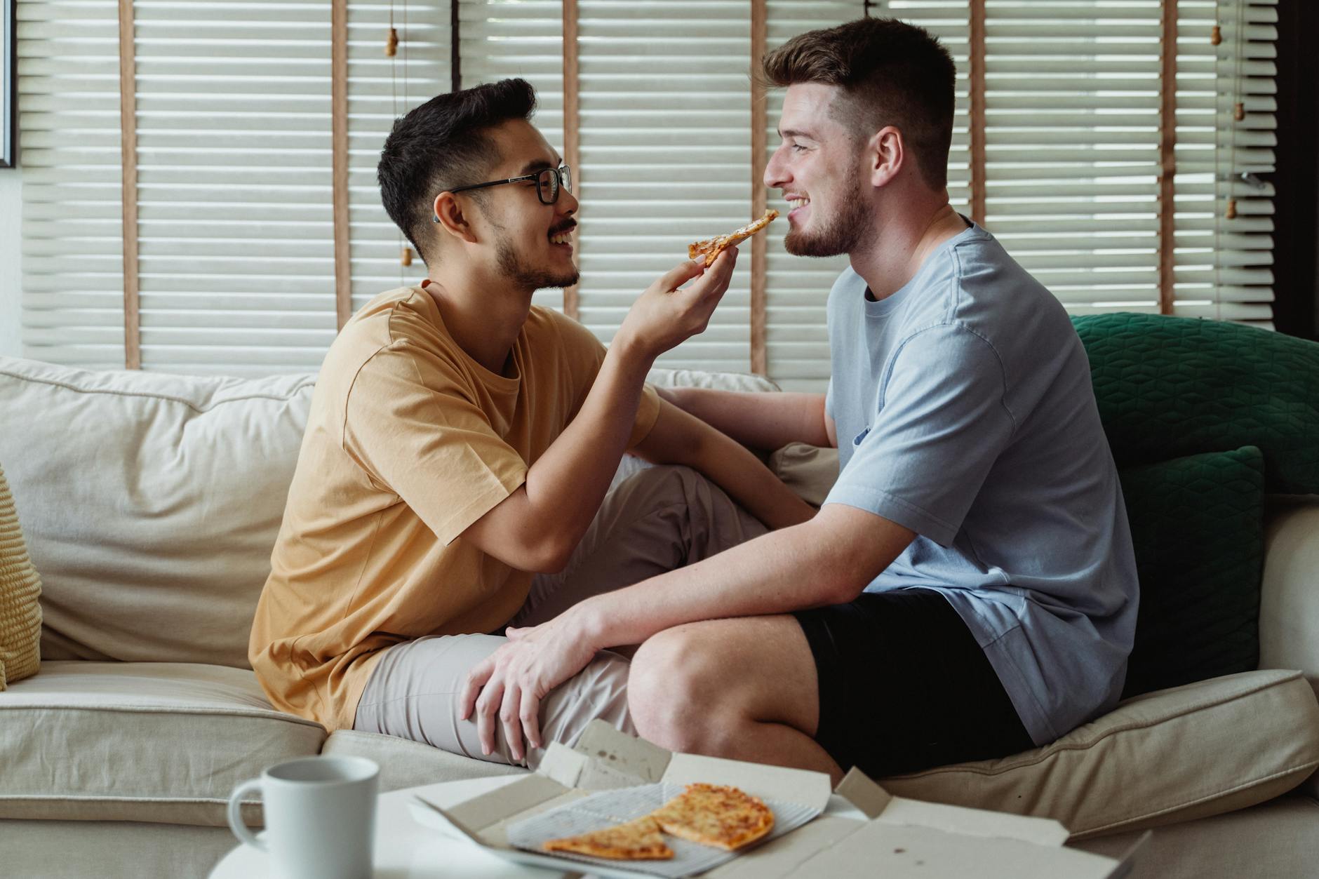 Happy interracial LGBT couple enjoying each other's company and pizza on a cozy sofa indoors. - rekindle intimacy couples