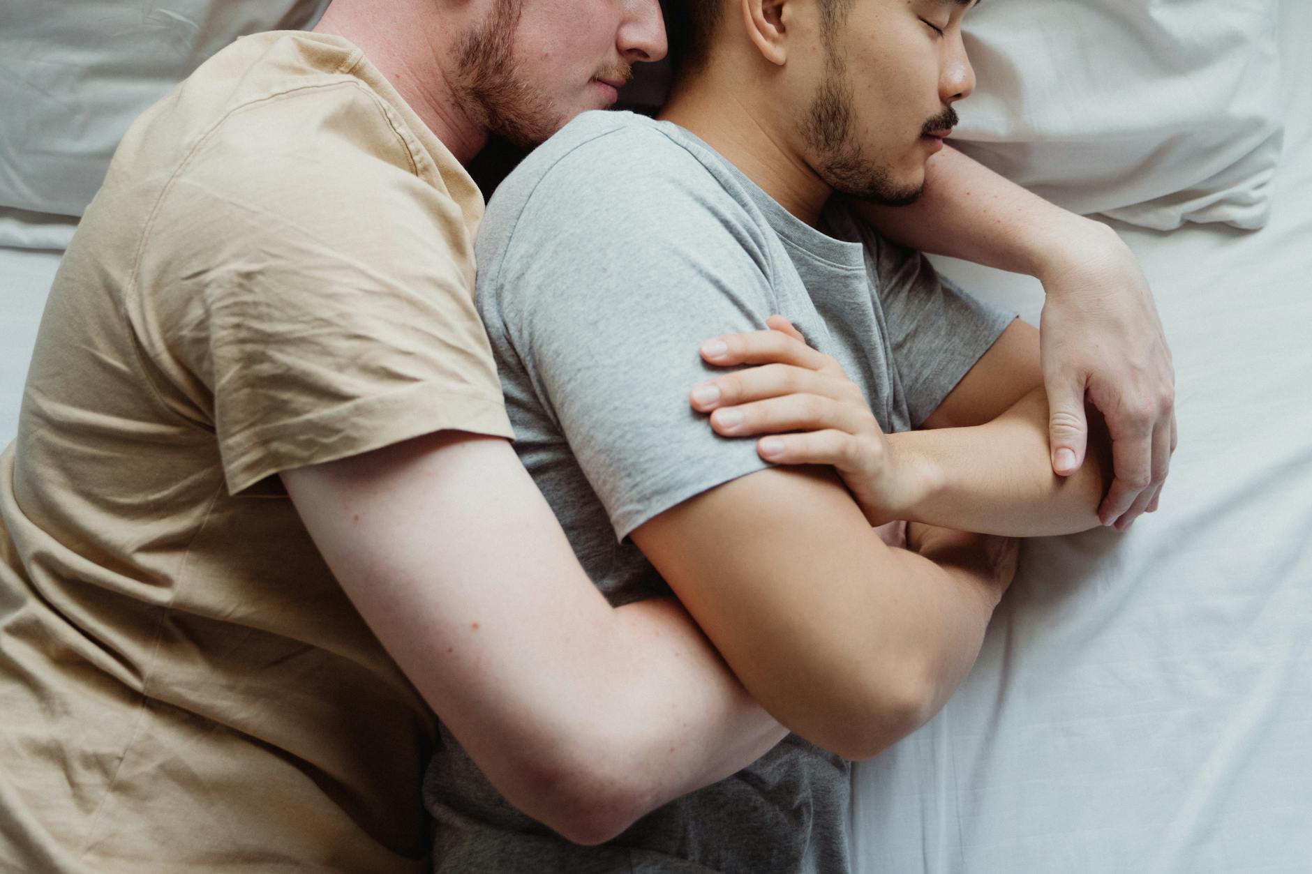 A tender moment between an interracial gay couple cuddling in bed, eyes closed, and relaxed. - rekindle intimacy couples