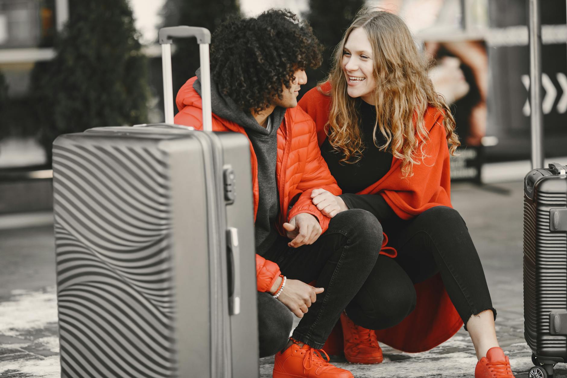 Smiling couple sitting with luggage, enjoying travel together in bold red outfits. - relationship emotional baggage