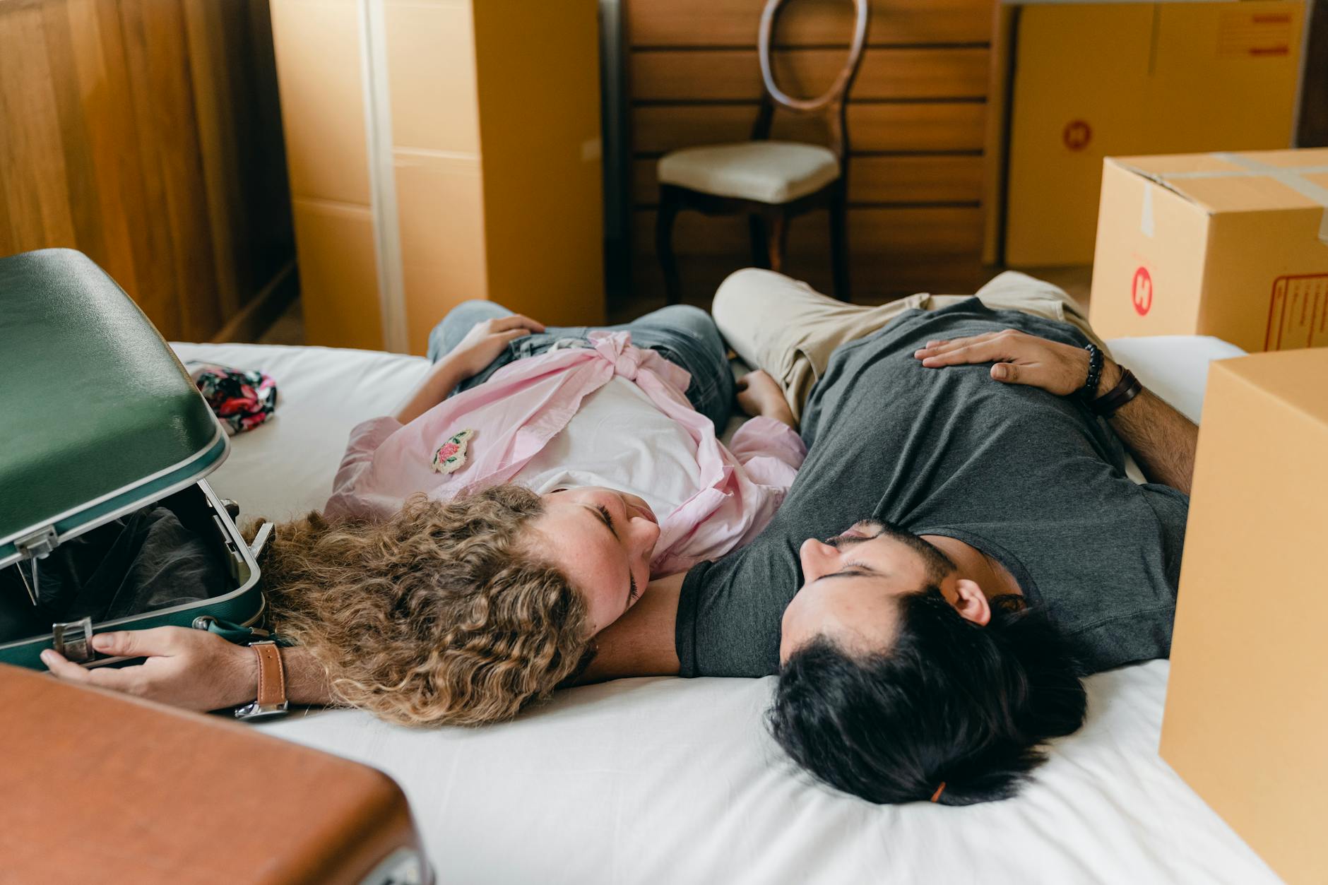 From above of diverse young couple in casual outfit hugging on bed between boxes and suitcases while resting together in modern bedroom during relocate - relationship emotional baggage