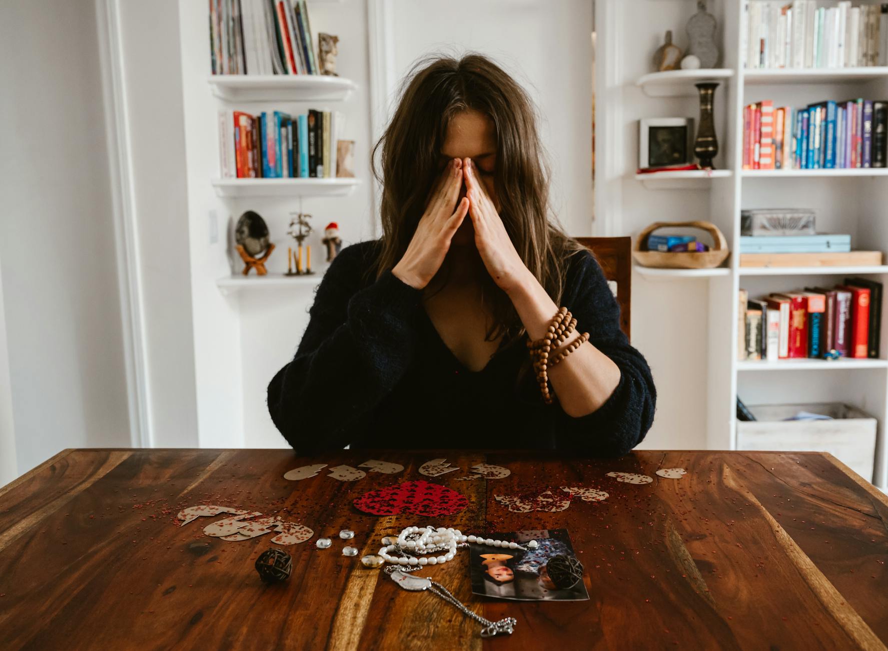 A woman in deep thought sits at a table with beads and a photo, conveying introspection. - relationship healing