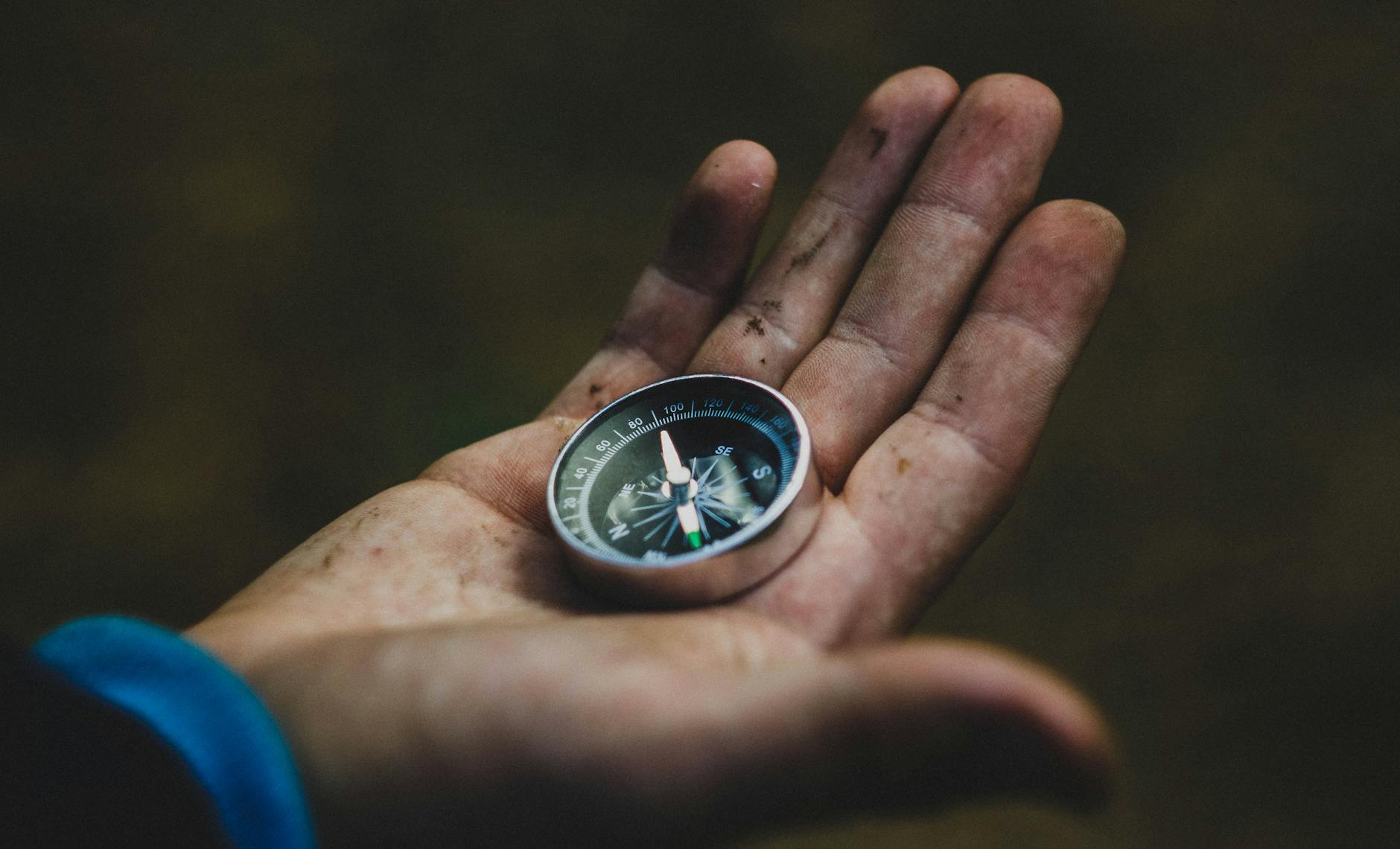 A close-up of a compass held in a dirty hand, symbolizing adventure and navigation. - self-compassion guide