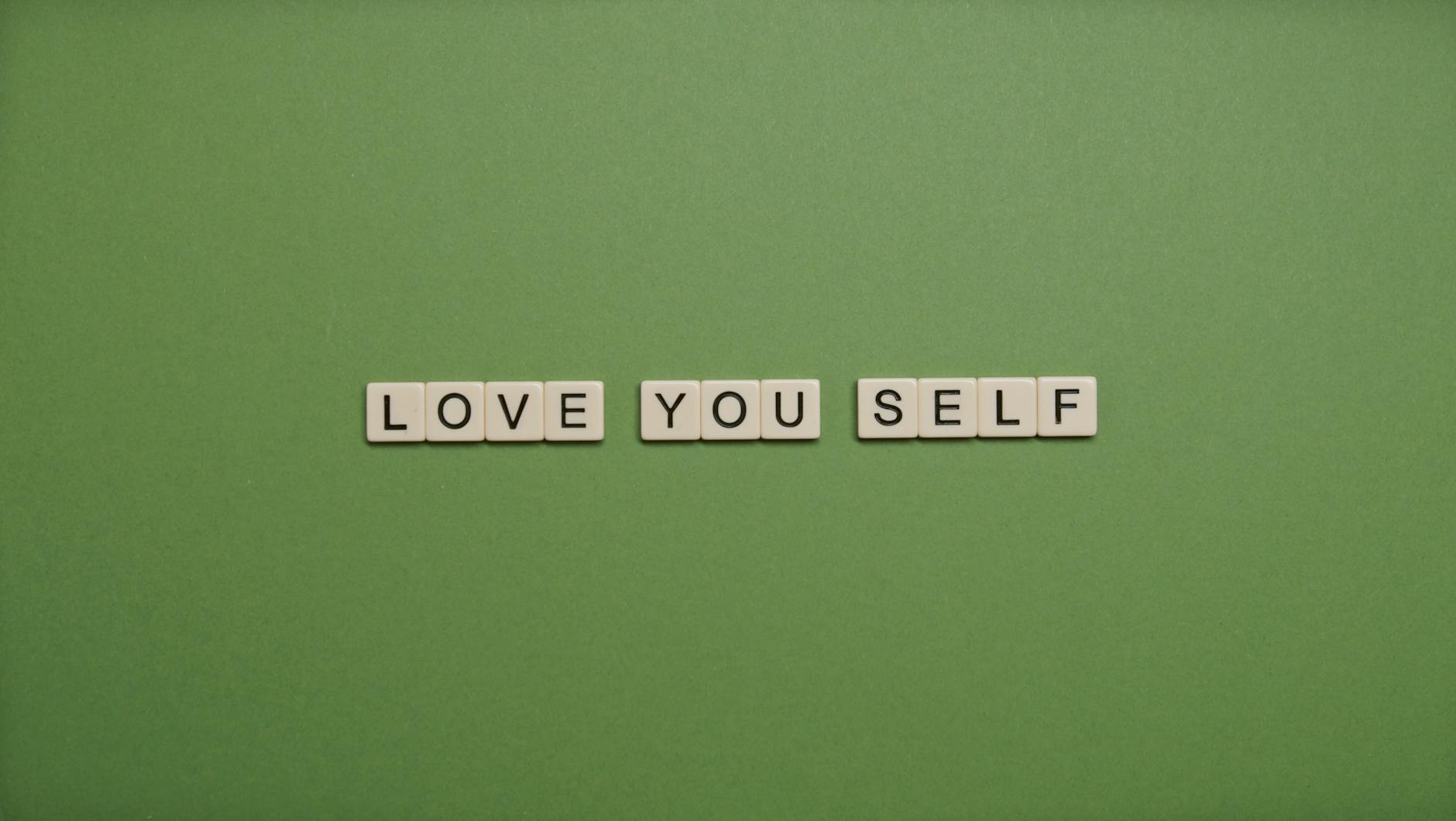 Positive message 'Love You Self' spelled with letter tiles on green background. - self compassion outdoors