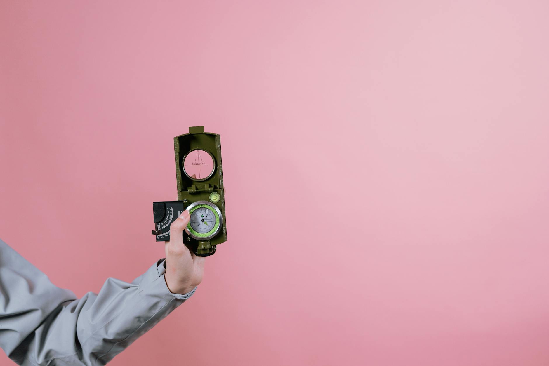 A person holds a military compass against a pink background, symbolizing navigation and direction. - self compassion outdoors