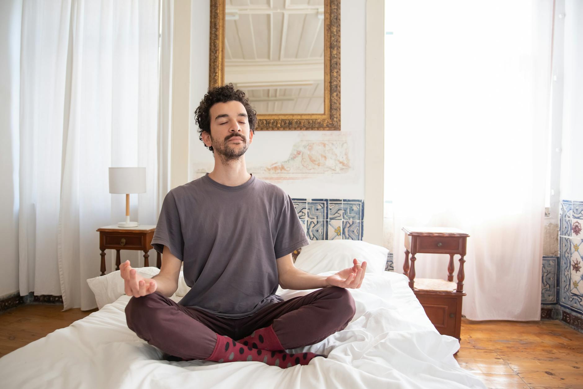 A man meditates calmly on a bed in a sunlit room, embracing tranquility and mindfulness. - self compassion spring