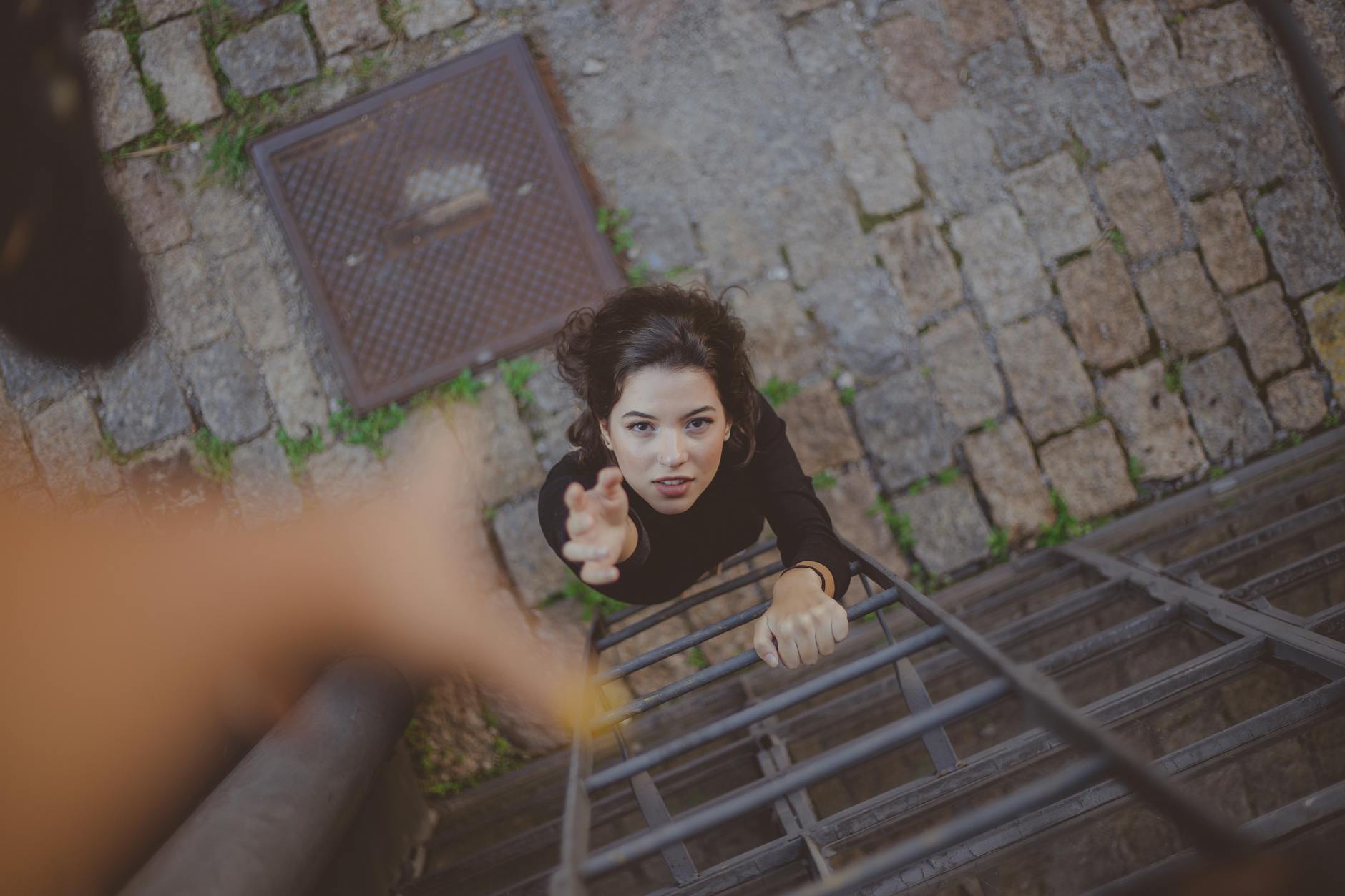 Woman climbs iron ladder outdoors, reaching for help with determination. - sexless marriage help