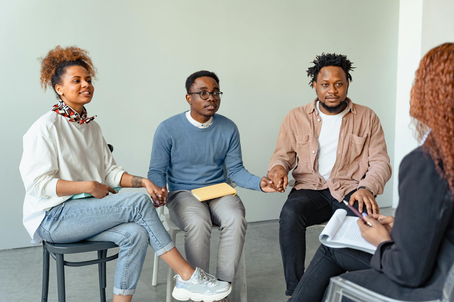 A diverse group of adults in a supportive therapy session, holding hands indoors. - social anxiety therapy