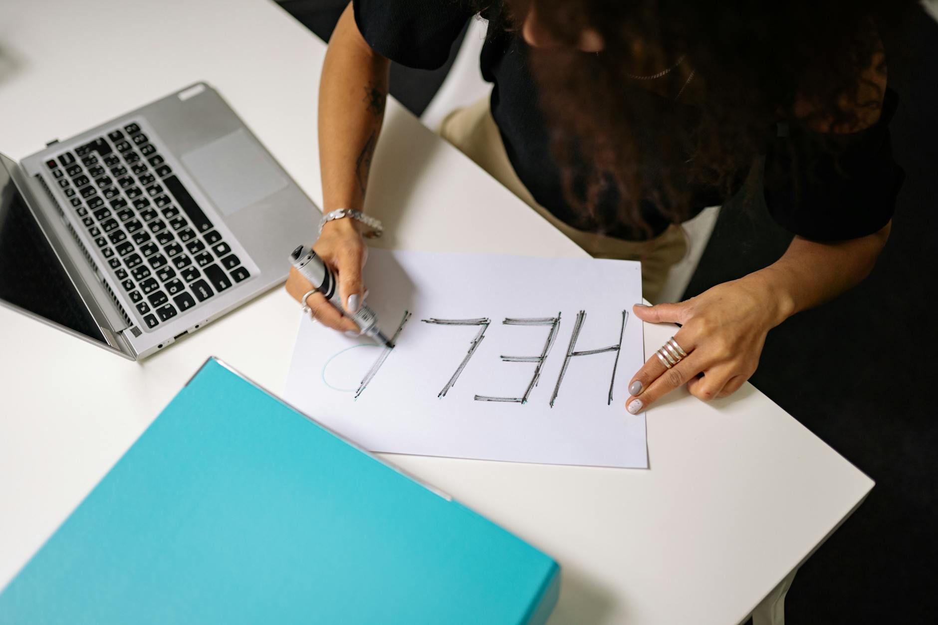 An overhead view of a woman writing 'HELP' on paper with a marker near a laptop. - spring anxiety help