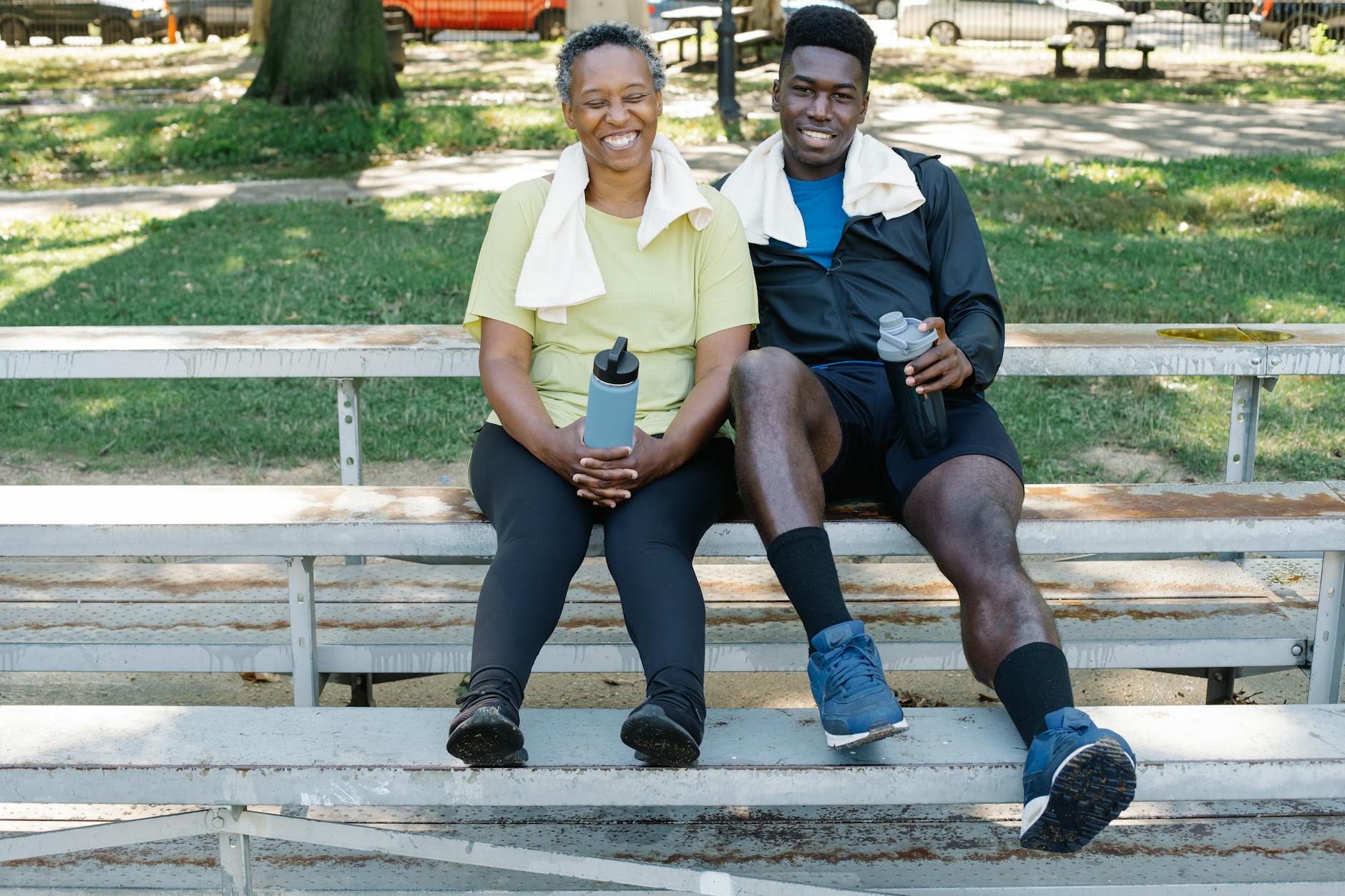 Mother and son in active wear relaxing on a park bench, drinking water bottles with post-exercise smiles. - spring break family boundaries