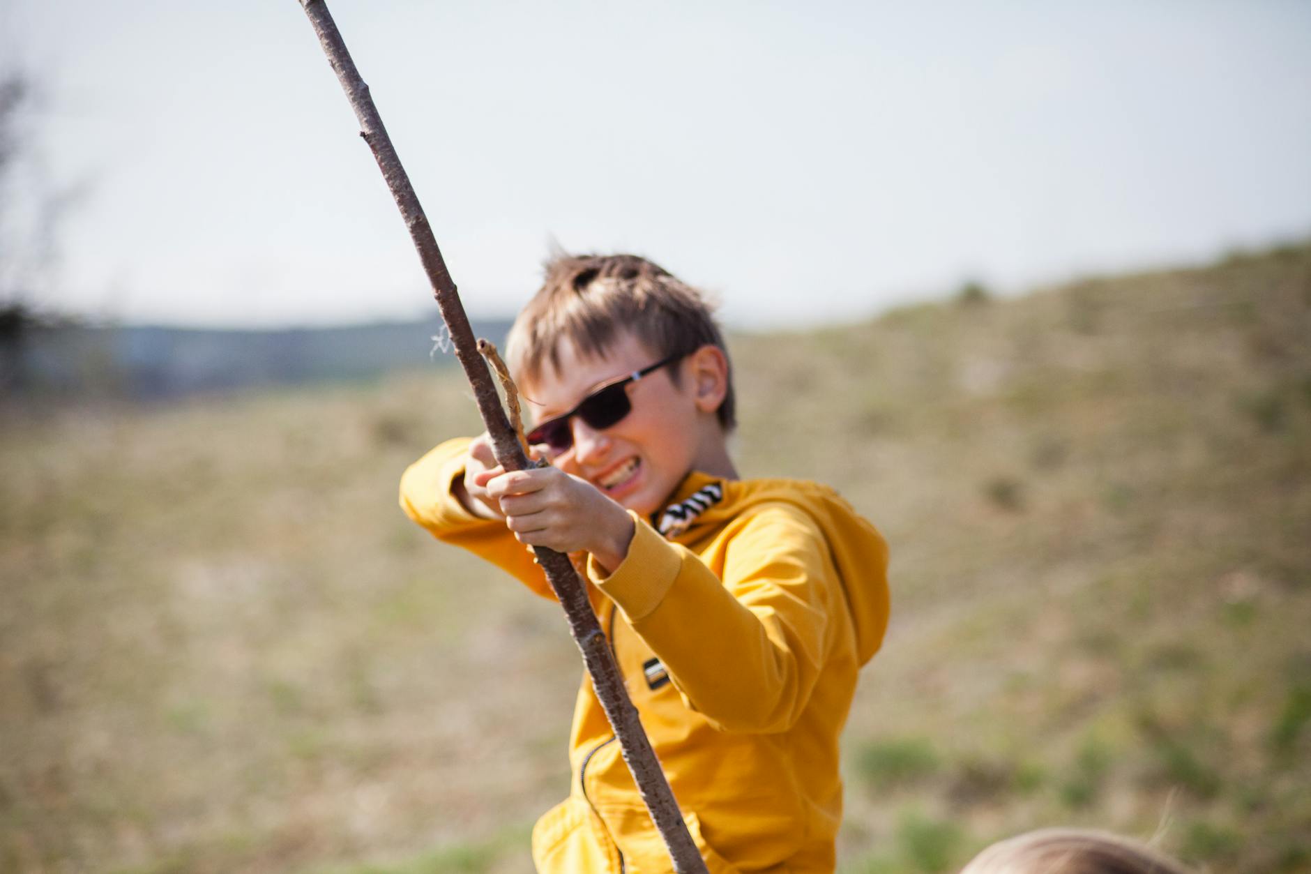 A happy child in sunglasses playing with a stick outdoors, capturing the essence of fun and energy. - spring child energy