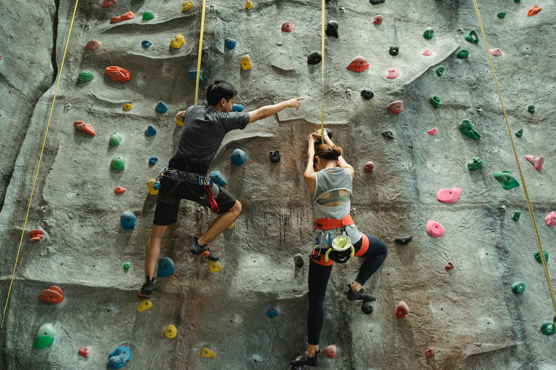 Back view of faceless mountaineers in sportswear with belay training climbing on wall - spring energy boost