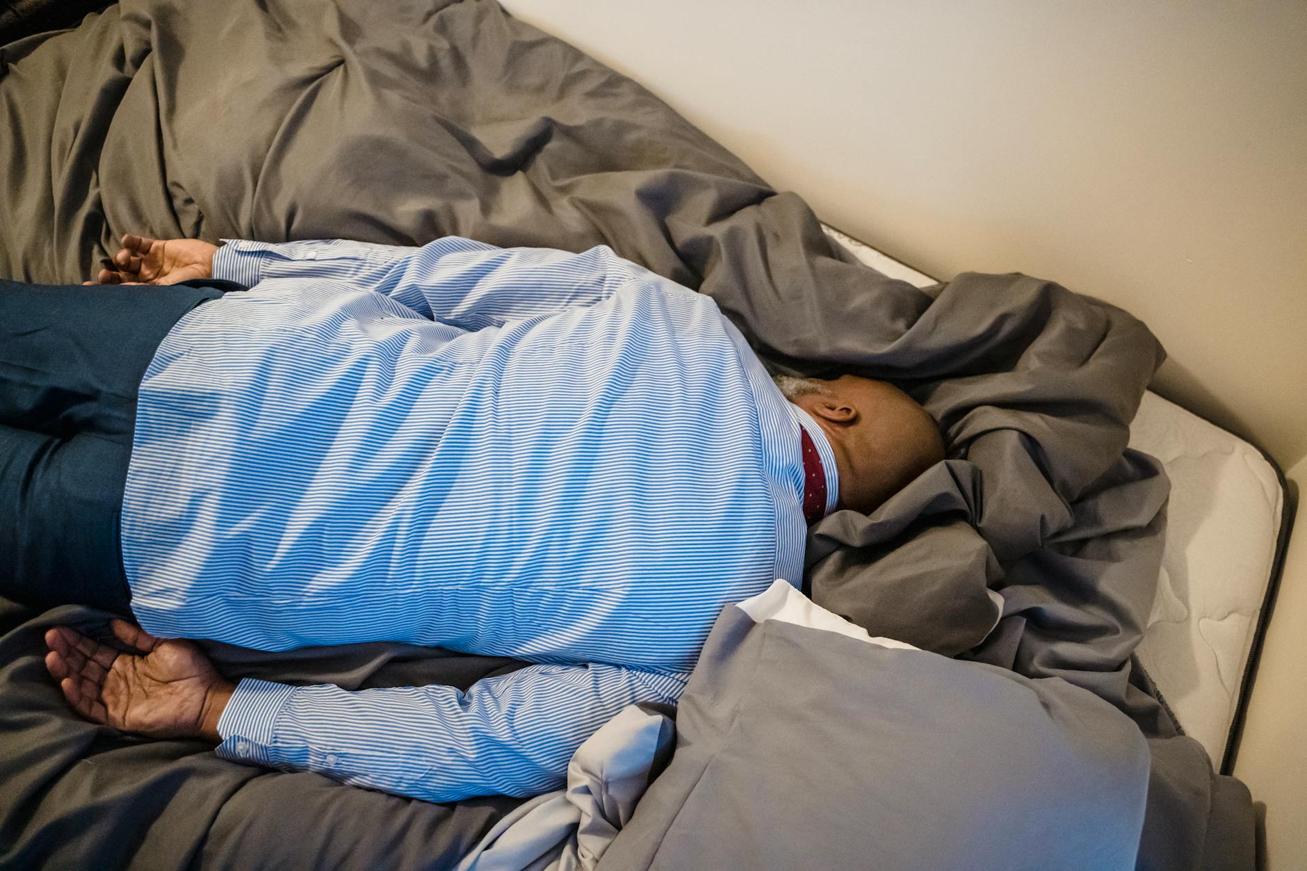 A man in formal attire rests face down on a bed, conveying exhaustion and fatigue. - spring fatigue causes