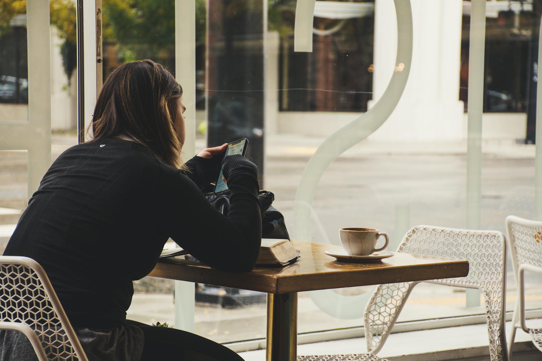 A woman enjoys coffee while using her smartphone at a cozy cafe table. - spring procrastination therapy