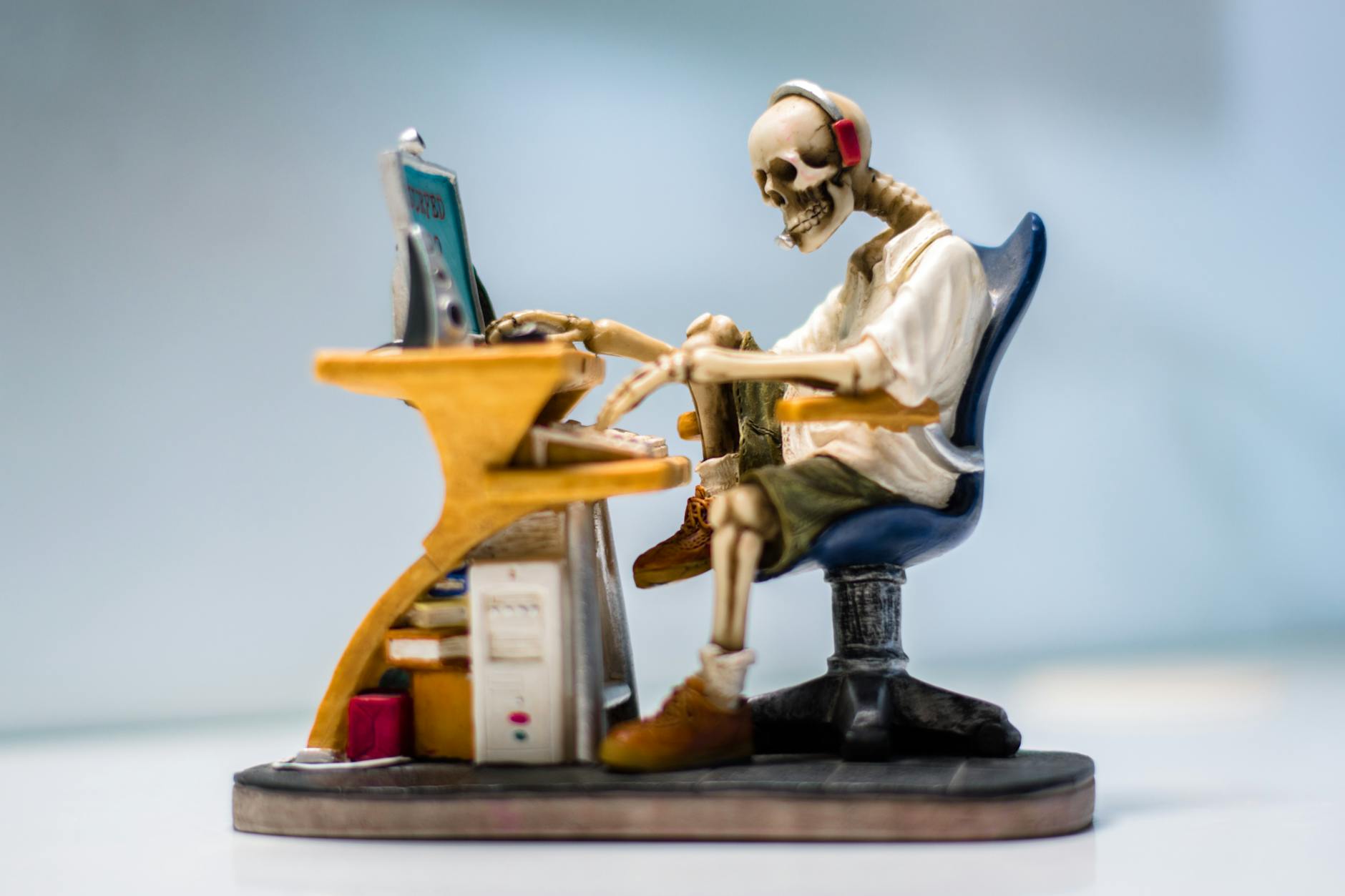 A quirky skeleton figurine wearing headphones sits at a desk with a computer, symbolizing burnout. - spring procrastination therapy