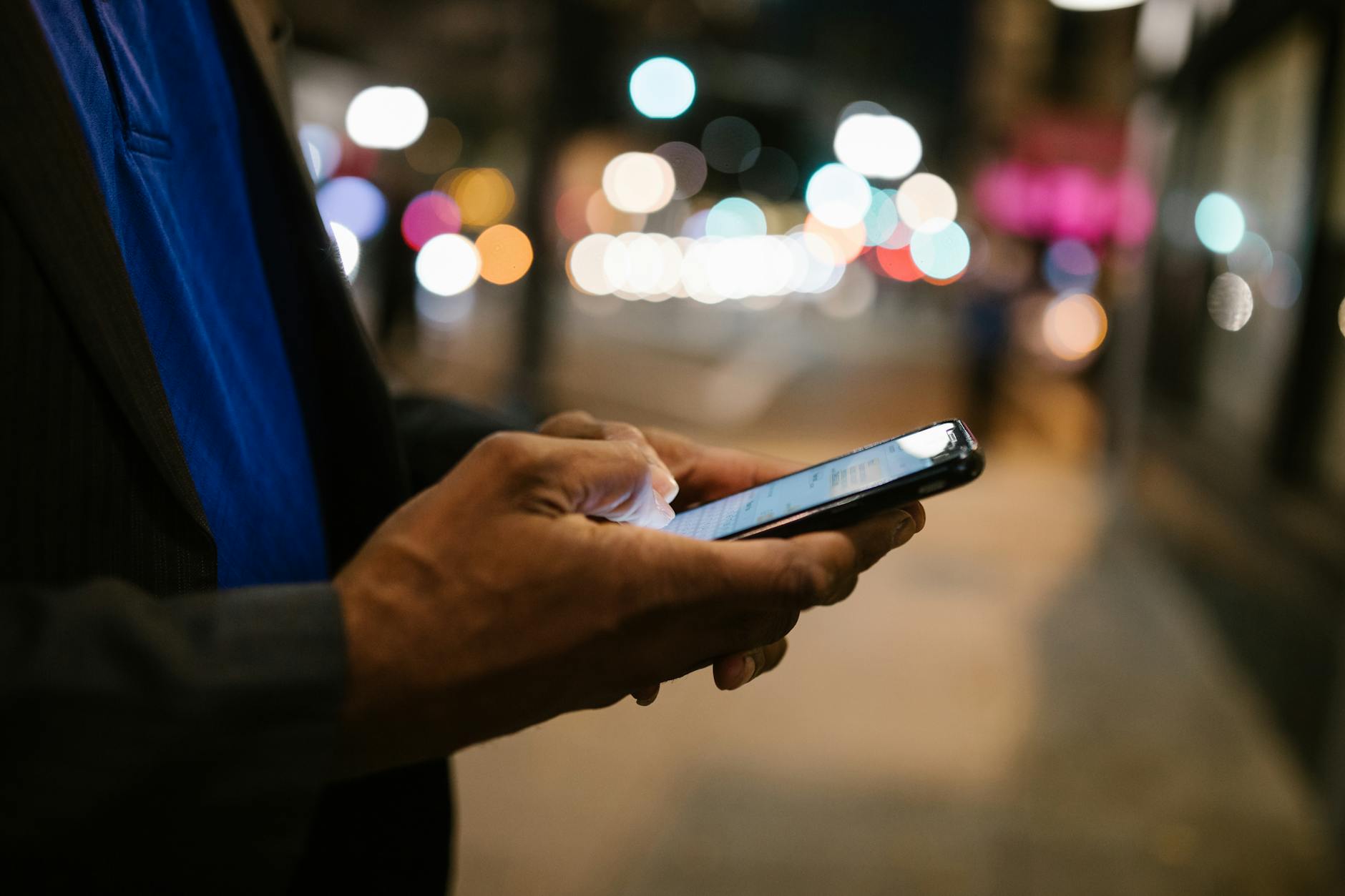 Close-up of a man using a smartphone on a busy city street at night. - spring relationship goals