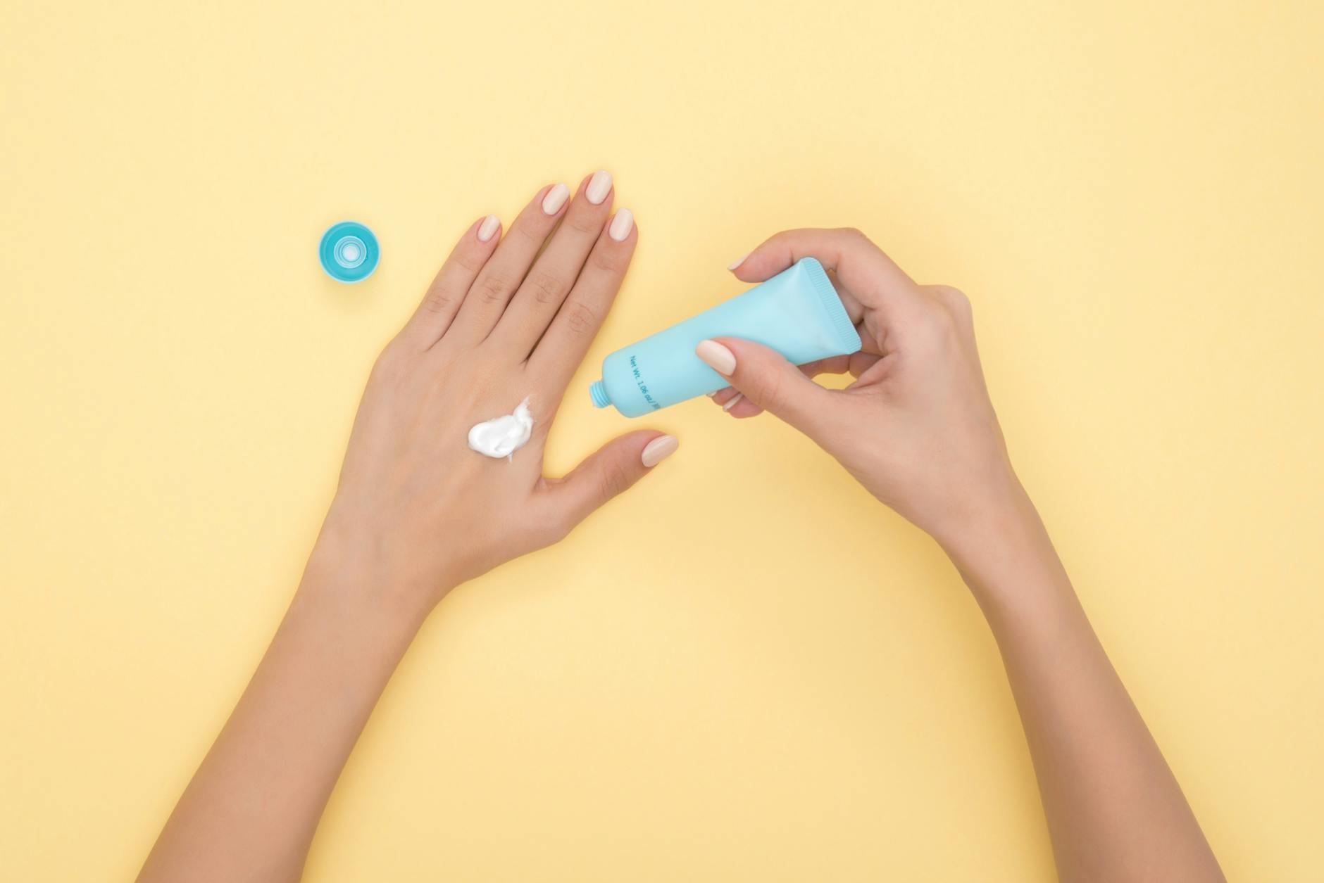 Close-up of a woman's hands applying cream on a pastel yellow background. Ideal for beauty and skincare themes. - spring self-care