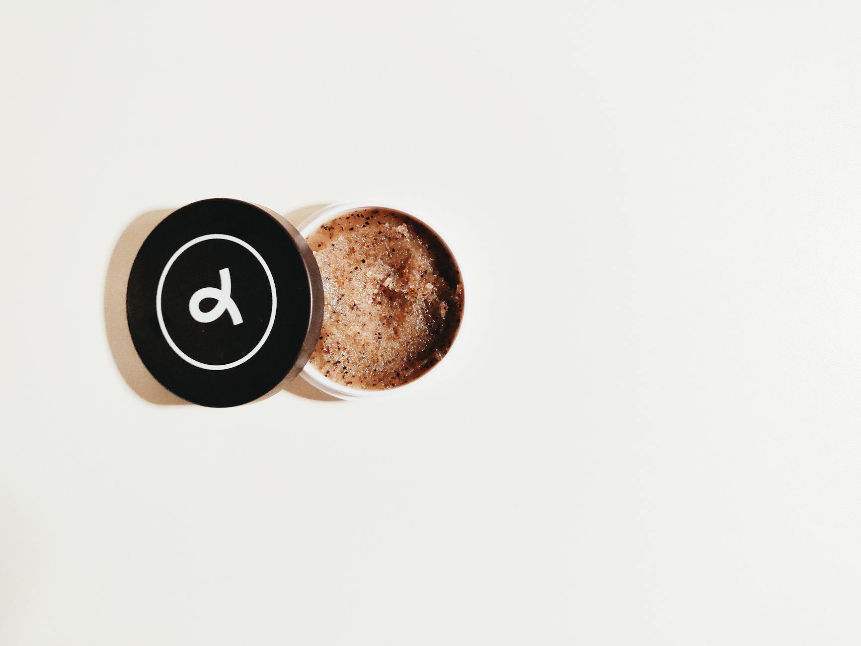 A minimalist photograph showcasing an open jar of coffee scrub on a clean white backdrop. - spring self-care